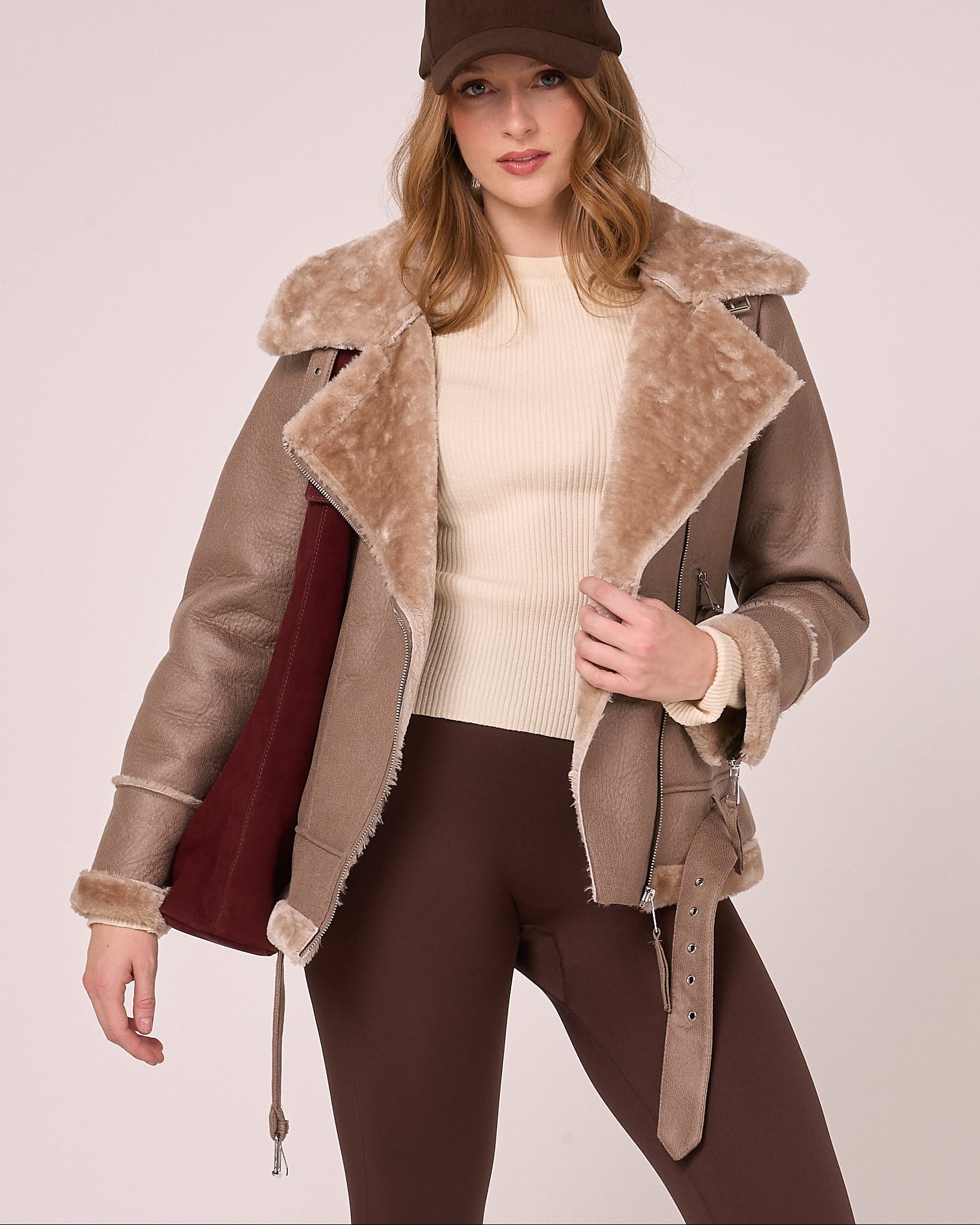 Woman wearing a brown faux shearling jacket with fur-lined collar on a plain background