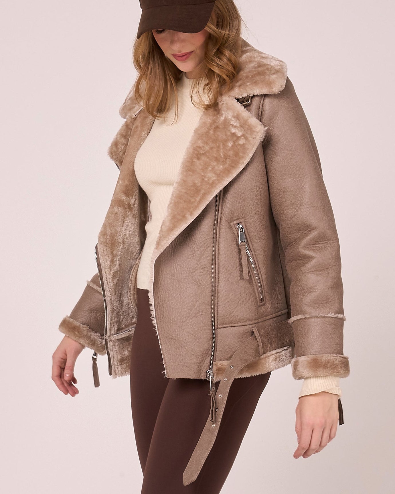 Woman wearing a beige jacket with faux fur trim on a plain background