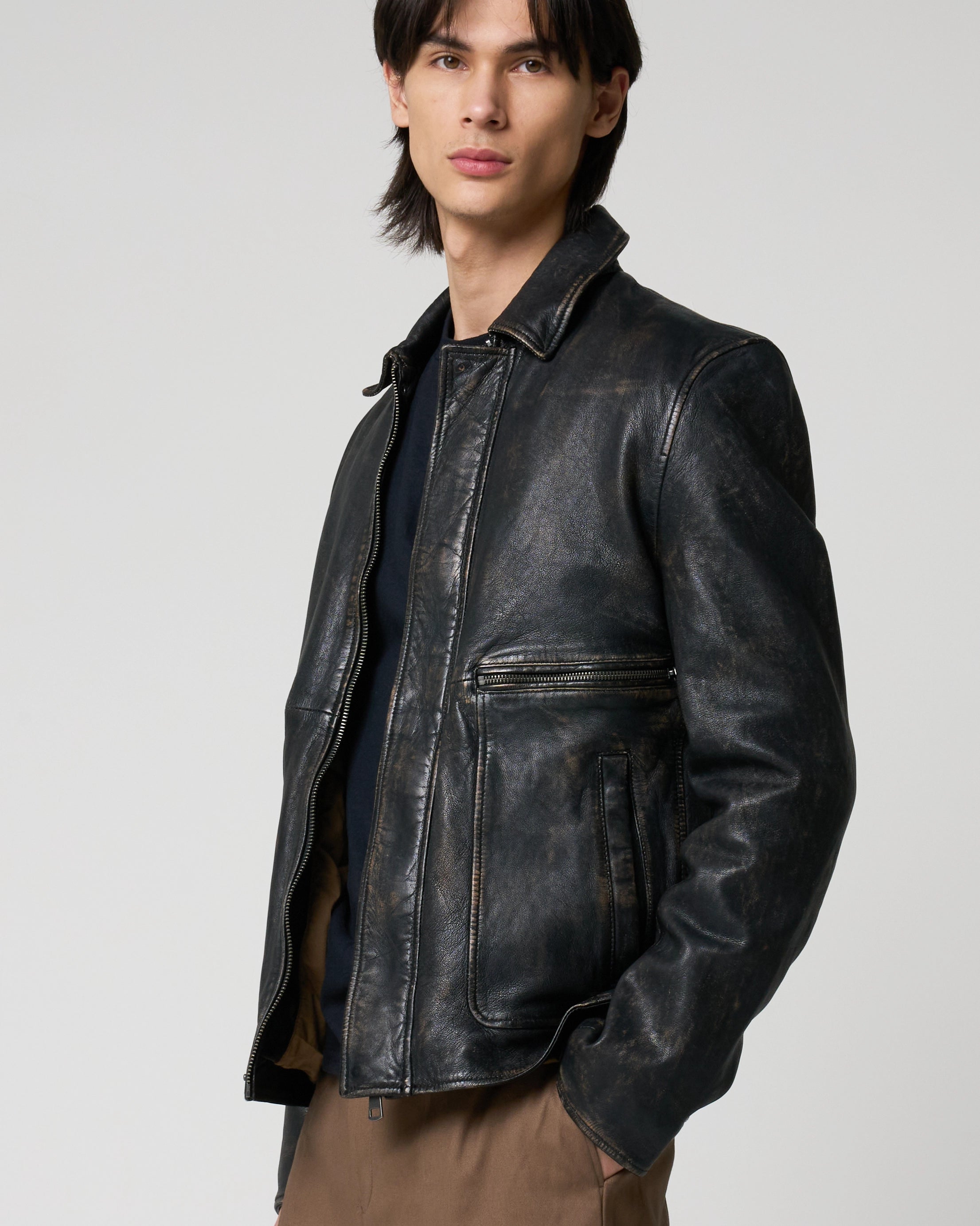 Man modelling a real leather jacket with collar, central zipline and zipper patch pockets.