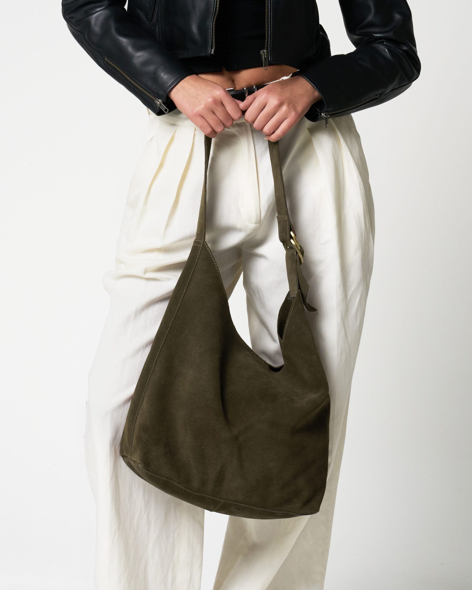 Person holding a green bag against a white background. The bag is made of real suede and has an adjustable d-ring strap.