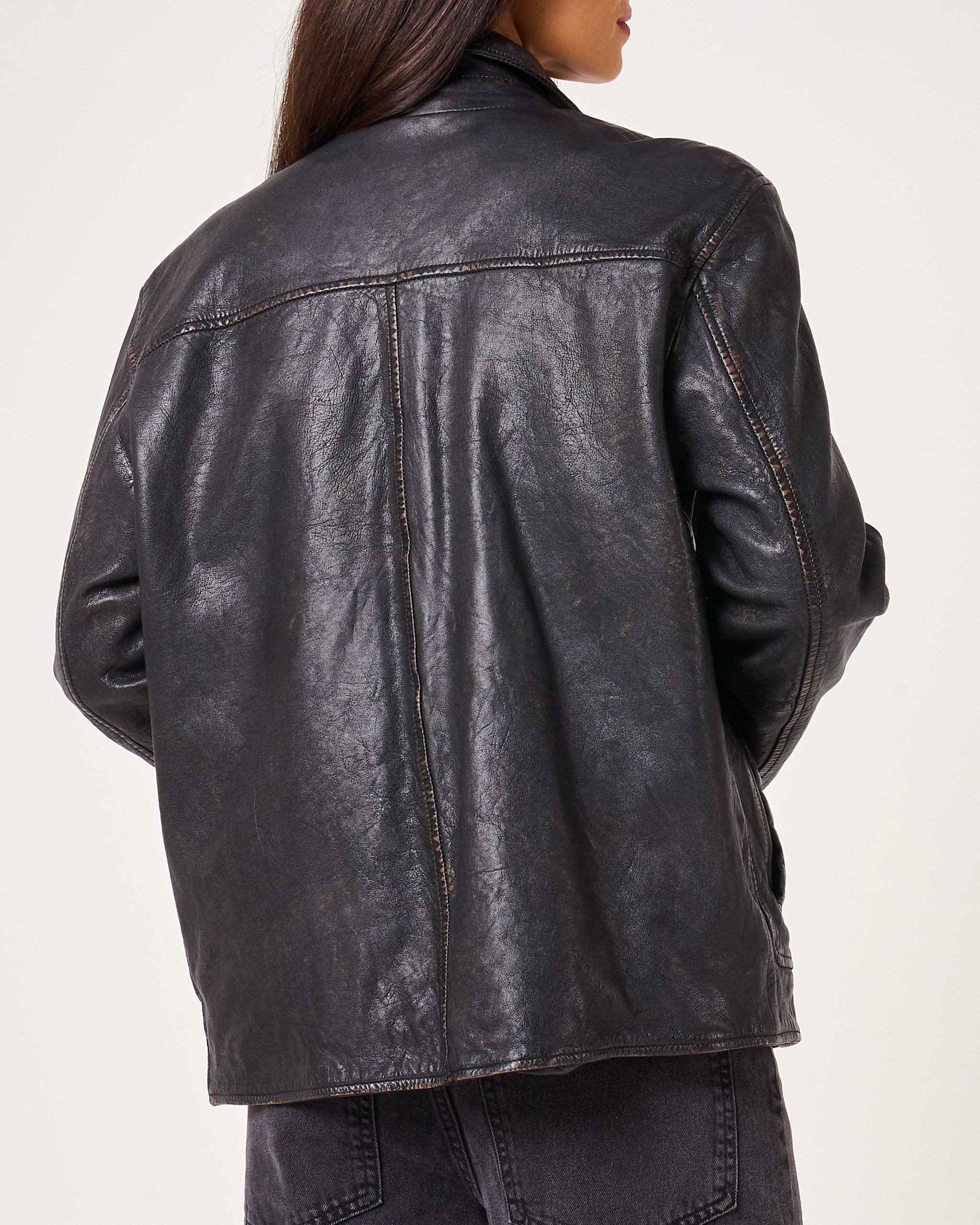 Back of leather jacket as worn by woman, there is a top horizontal seem and a vertical seem in the center: no logos or pattern.