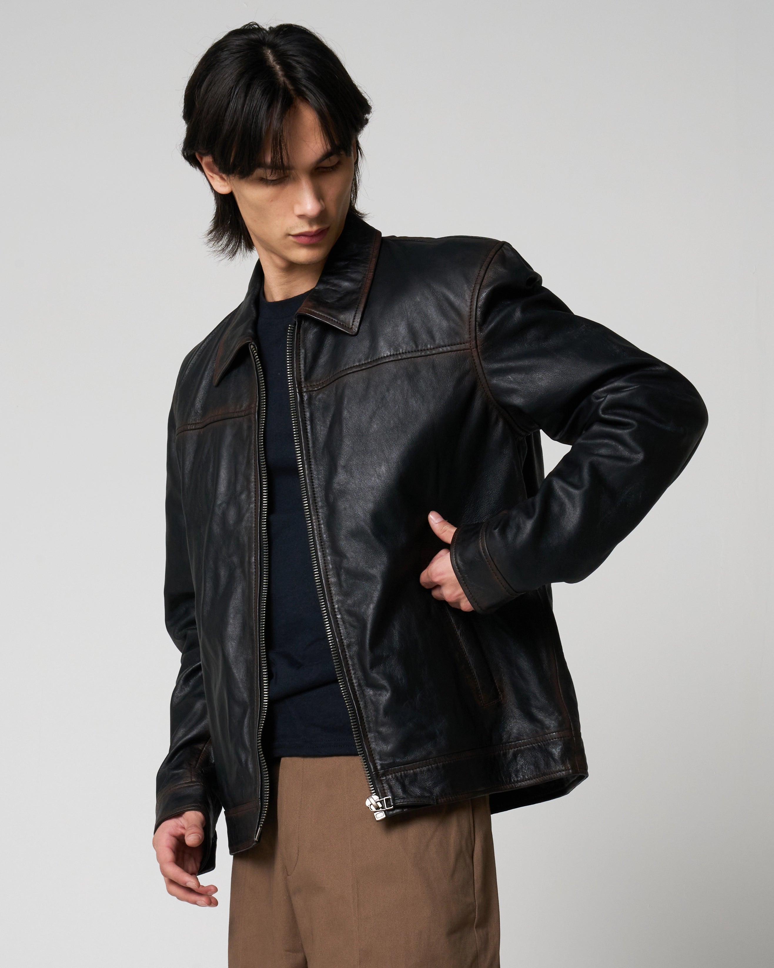 Man wearing a real leather jacket with rust washed detail. He turns to place his hand in the pocket.