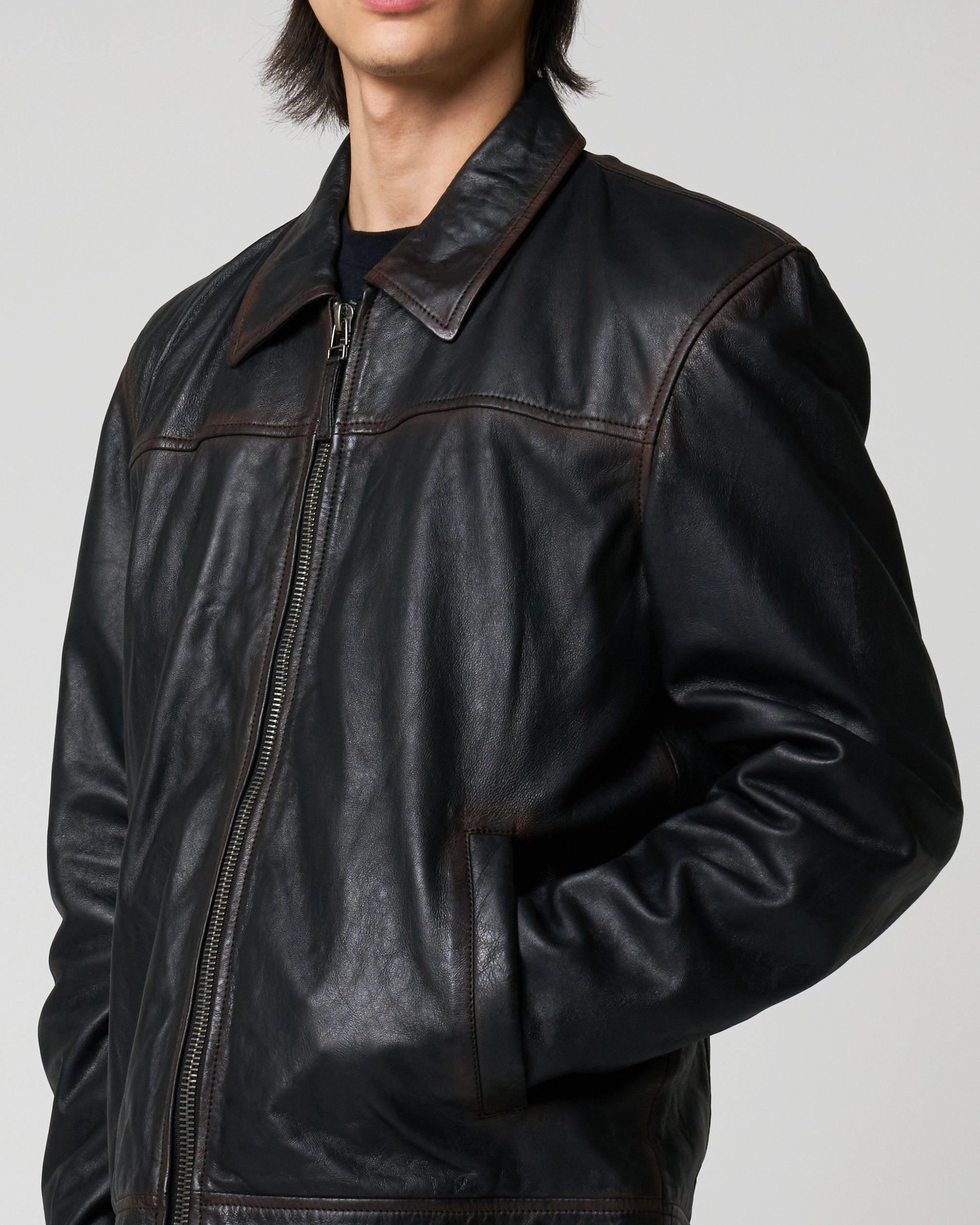 A close-up of a person wearing a black leather jacket with dark brown contrast washed detail which runs across the seem lines.