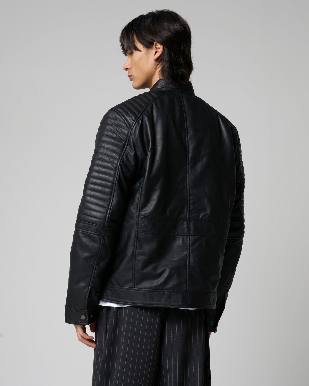 Image shows the back of the real leather racer jacket as worn by a male model. The sleeves have ribbed detail that runs down to the elbow area.