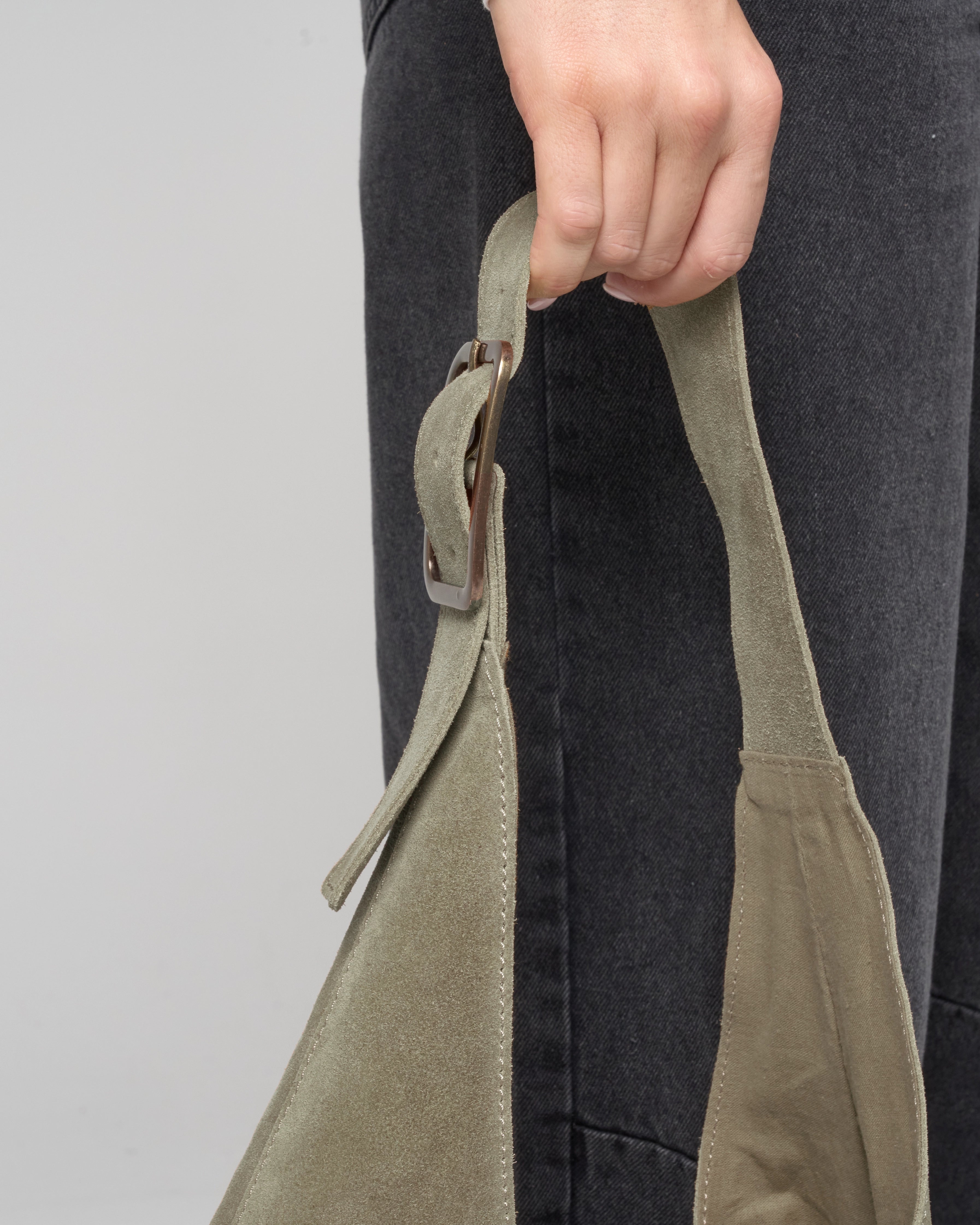 Close up detail image of olive suede slouch bag handle as held by woman model.