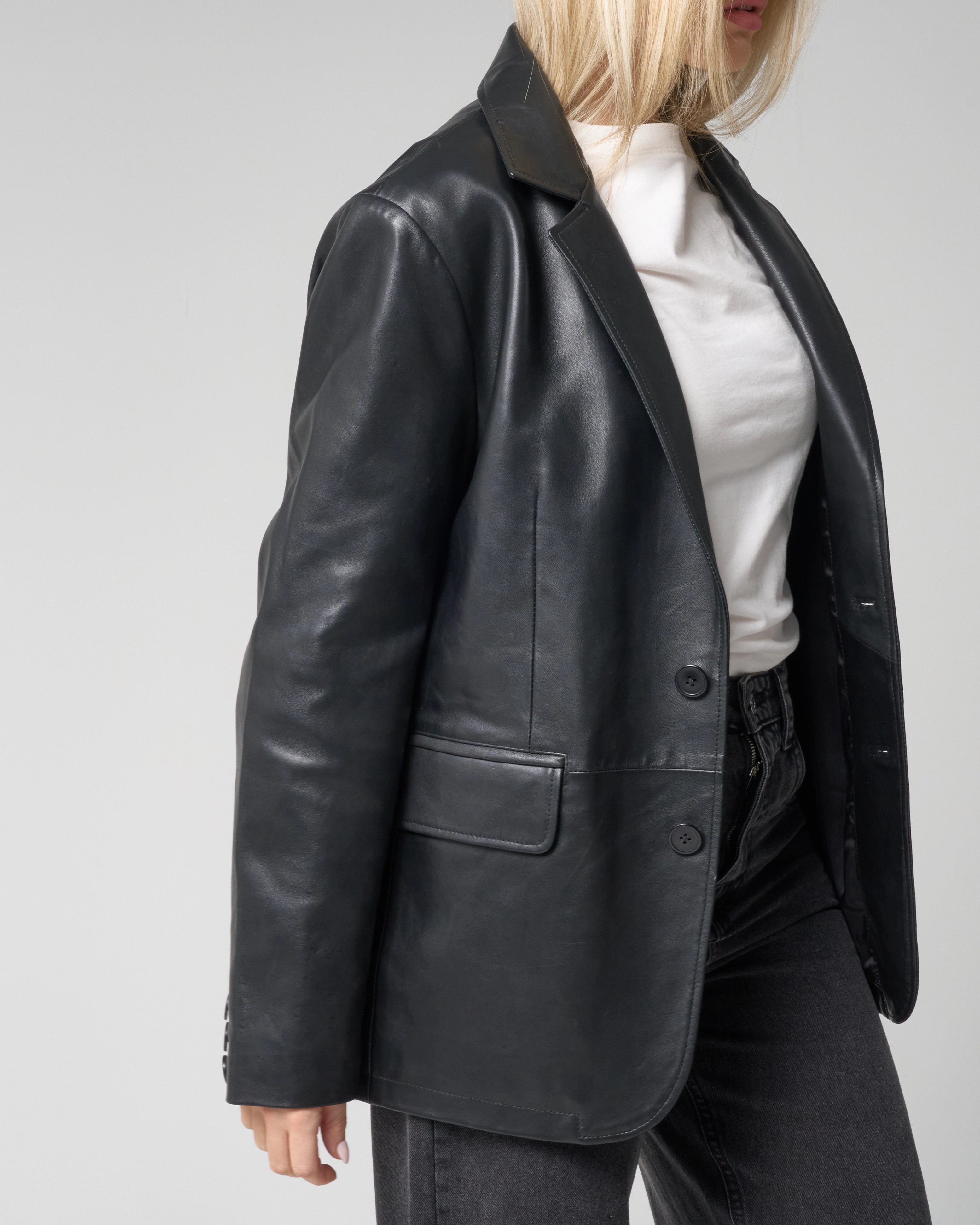 Close up crop of side profile featuring the black leather blazer jacket from Barneys Originals. The blazer is worn open, unbuttoned and the image focuses on the lower waist pocket.