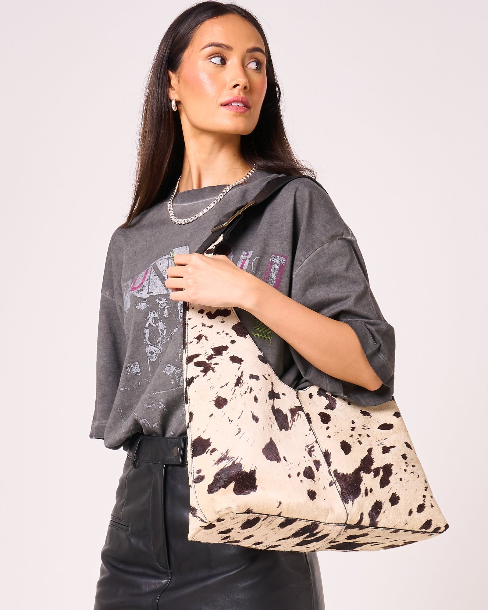 Woman carries cow print slouch bag over her shoulder.