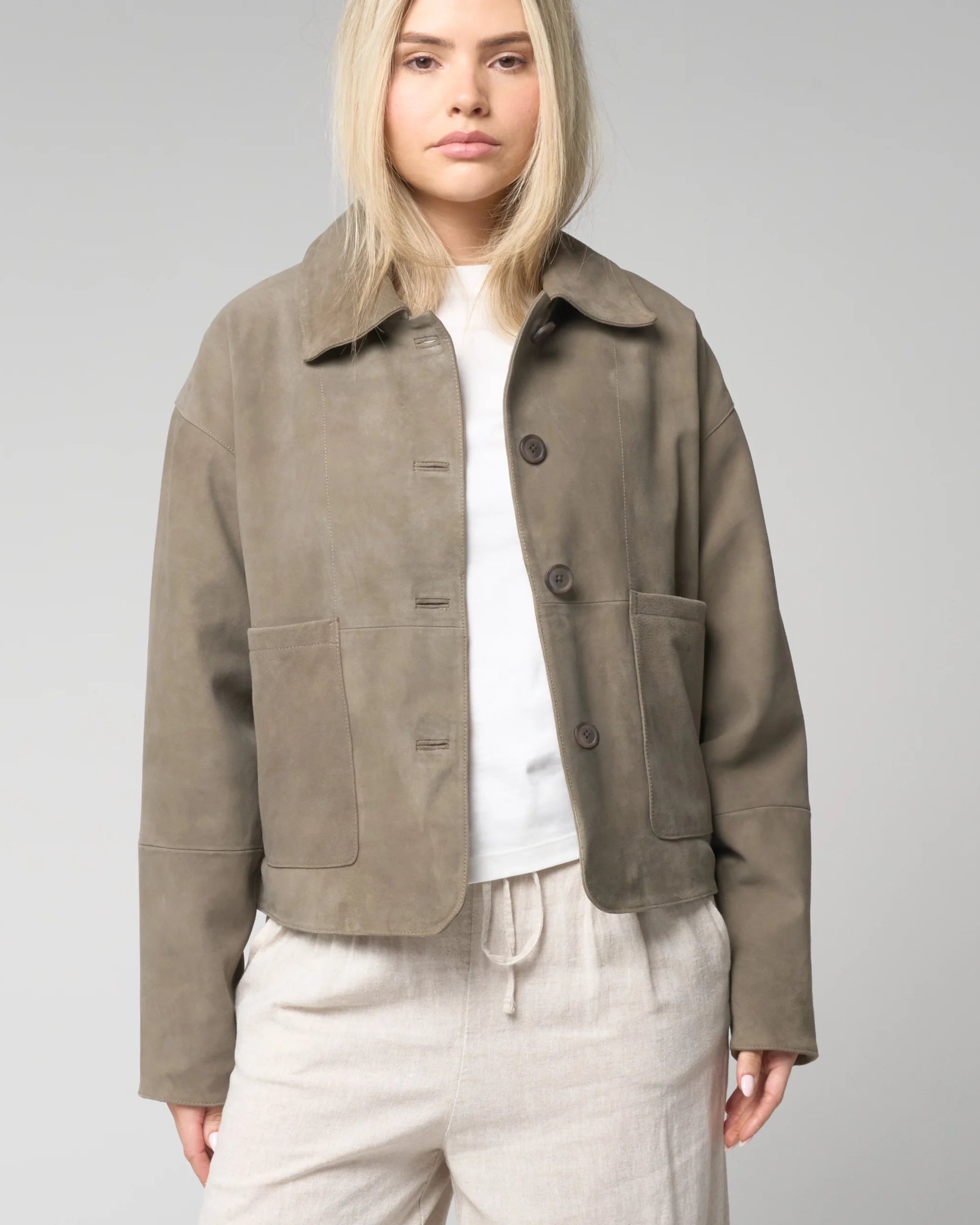 Close up image of woman wearing a suede jacket with buttons which is sage green in colour. It has a soft and smooth textural appearance.