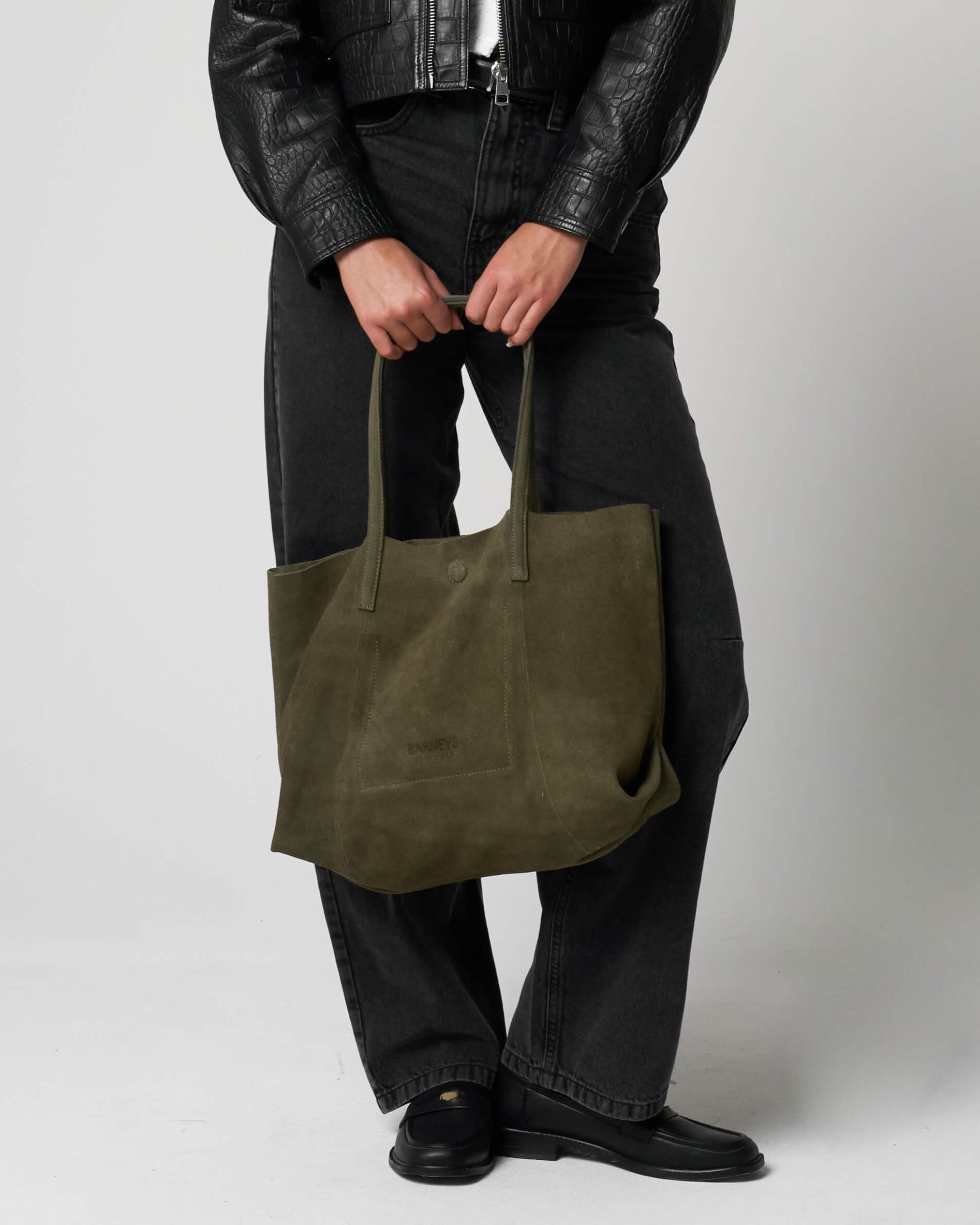 Person holding a green tote bag made from suede against a plain background