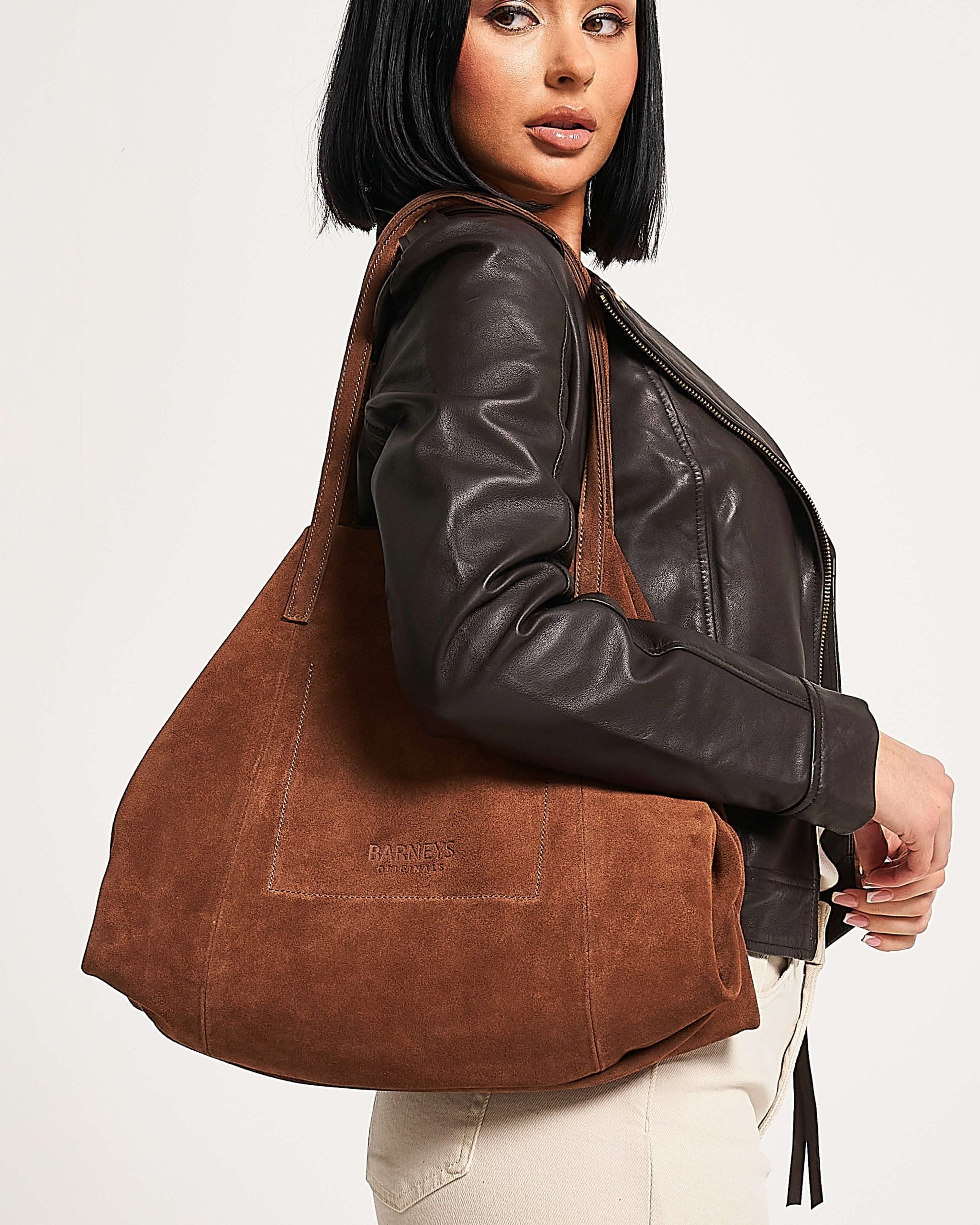 Woman holding a tan suede handbag with a visible brand logo - Barneys Originals.
