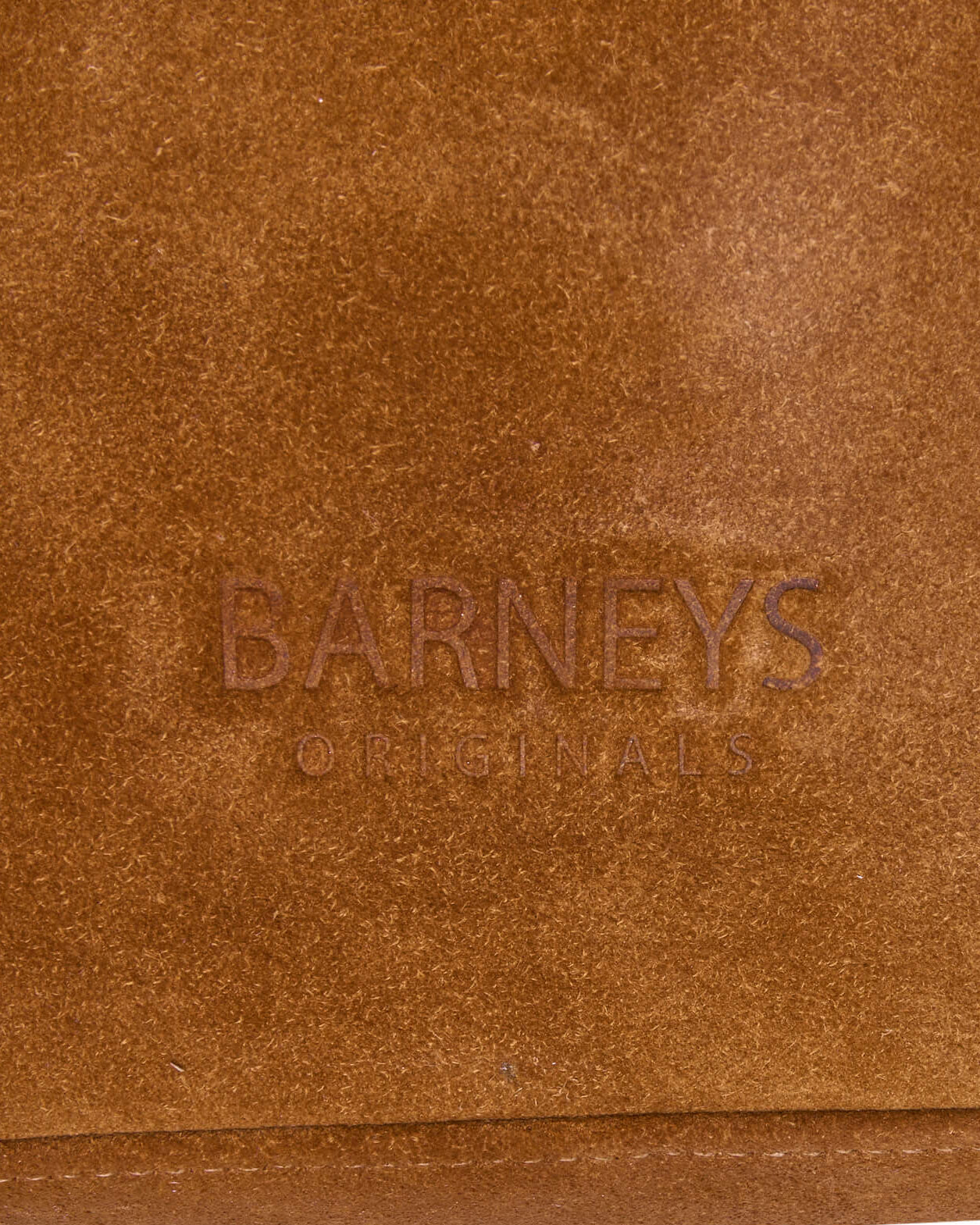 Cropped image focusing on the embossed branded detailing on the real suede bag. The words embossed into the material are 'Barneys Originals'.