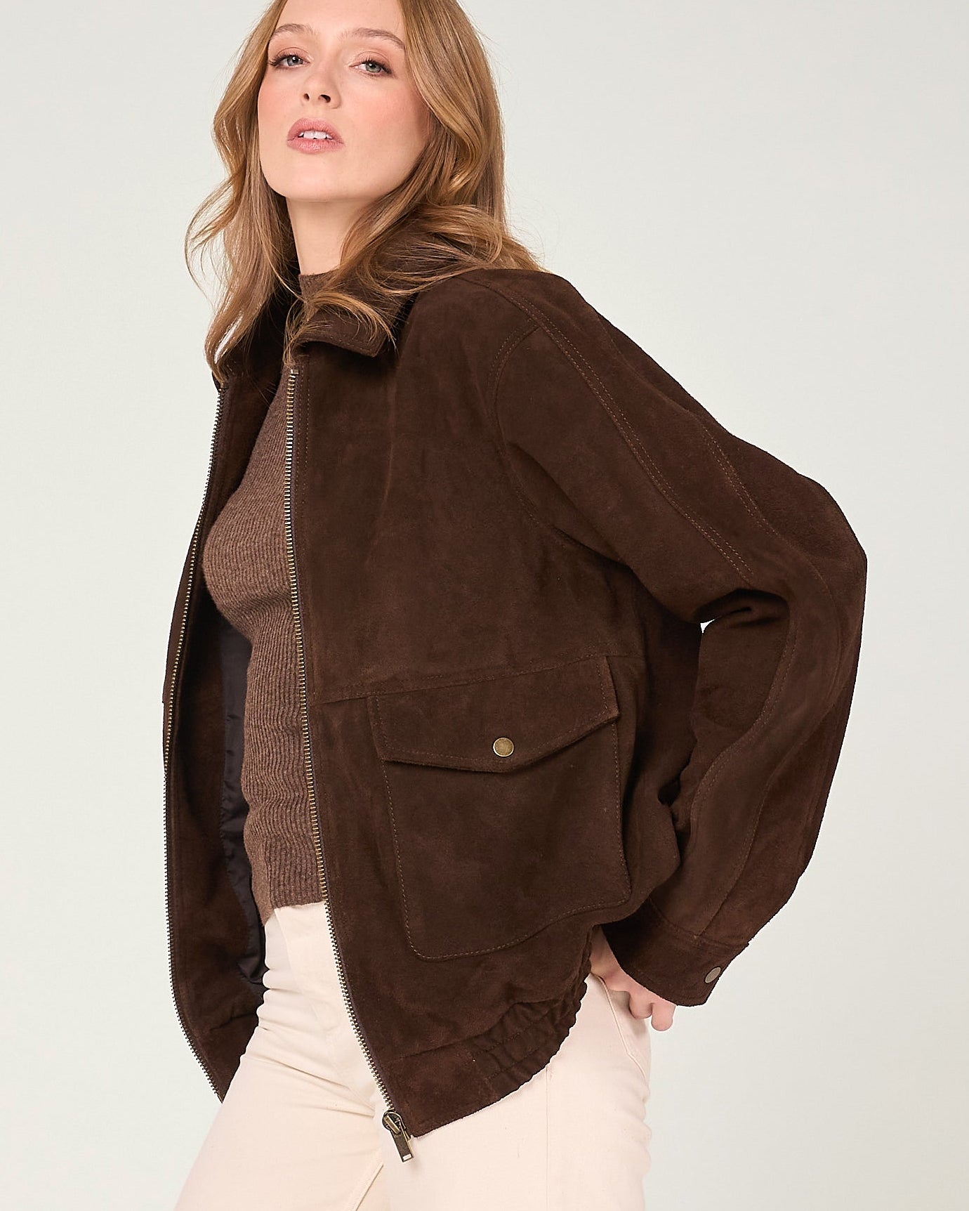 Woman wearing a brown jacket over a sweater and pants on a white background