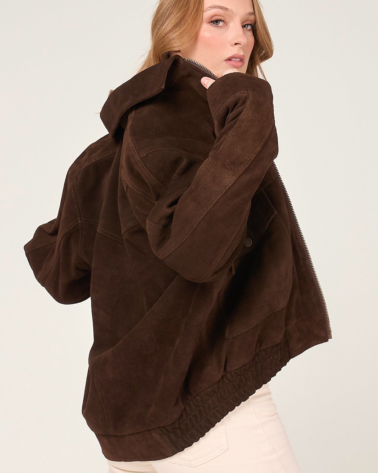 Woman wearing a brown suede bomber jacket on a plain background