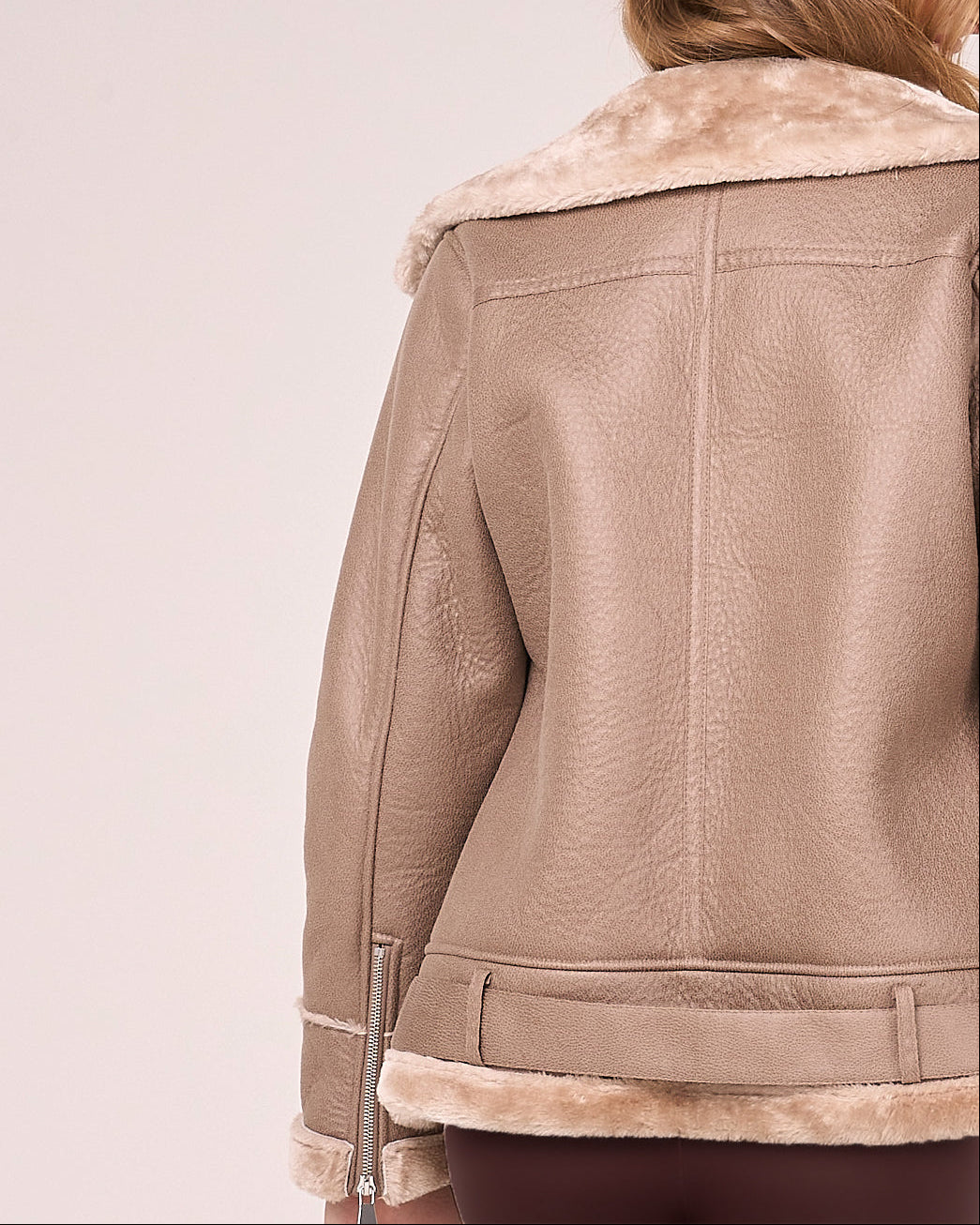 Image shows the bag of the beige faux shearling jacket from Barneys Originals. There is a belt and central seem. The back of the sleeves feature a zipper.