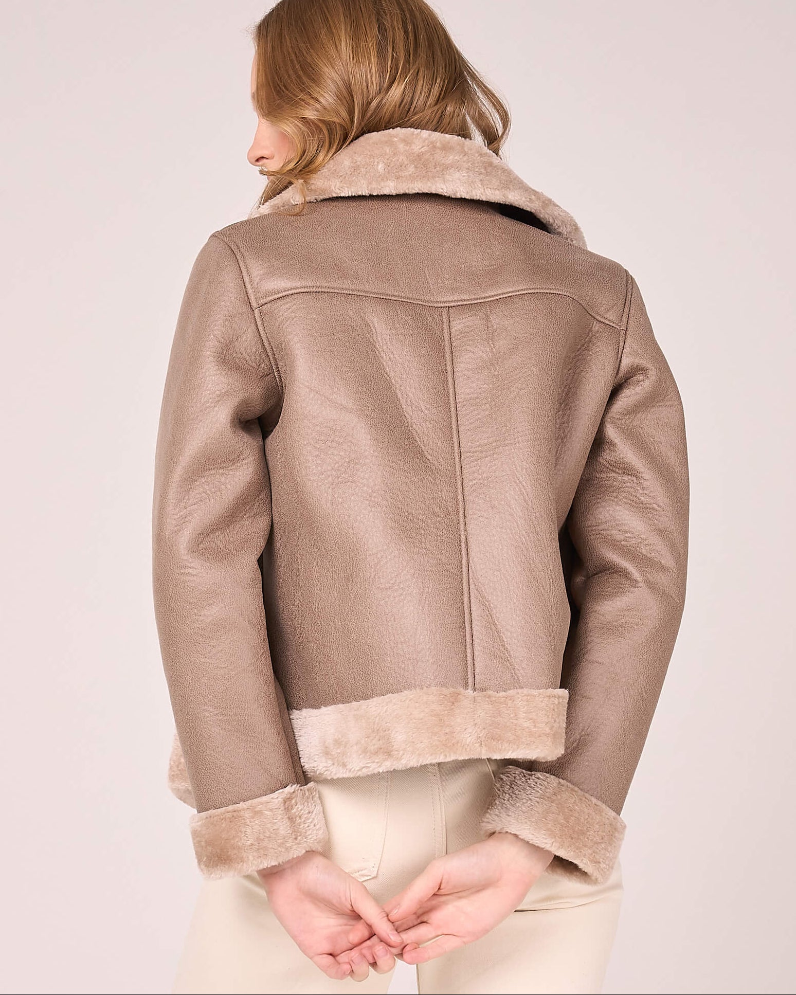 Person wearing a beige shearling jacket on a plain background