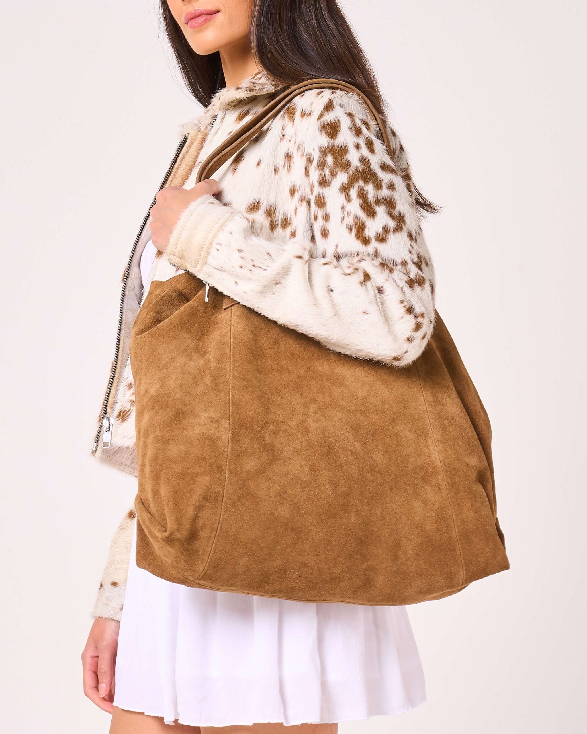 Side on image of a sandy suede tote bag as woman by a model over the shoulder.
