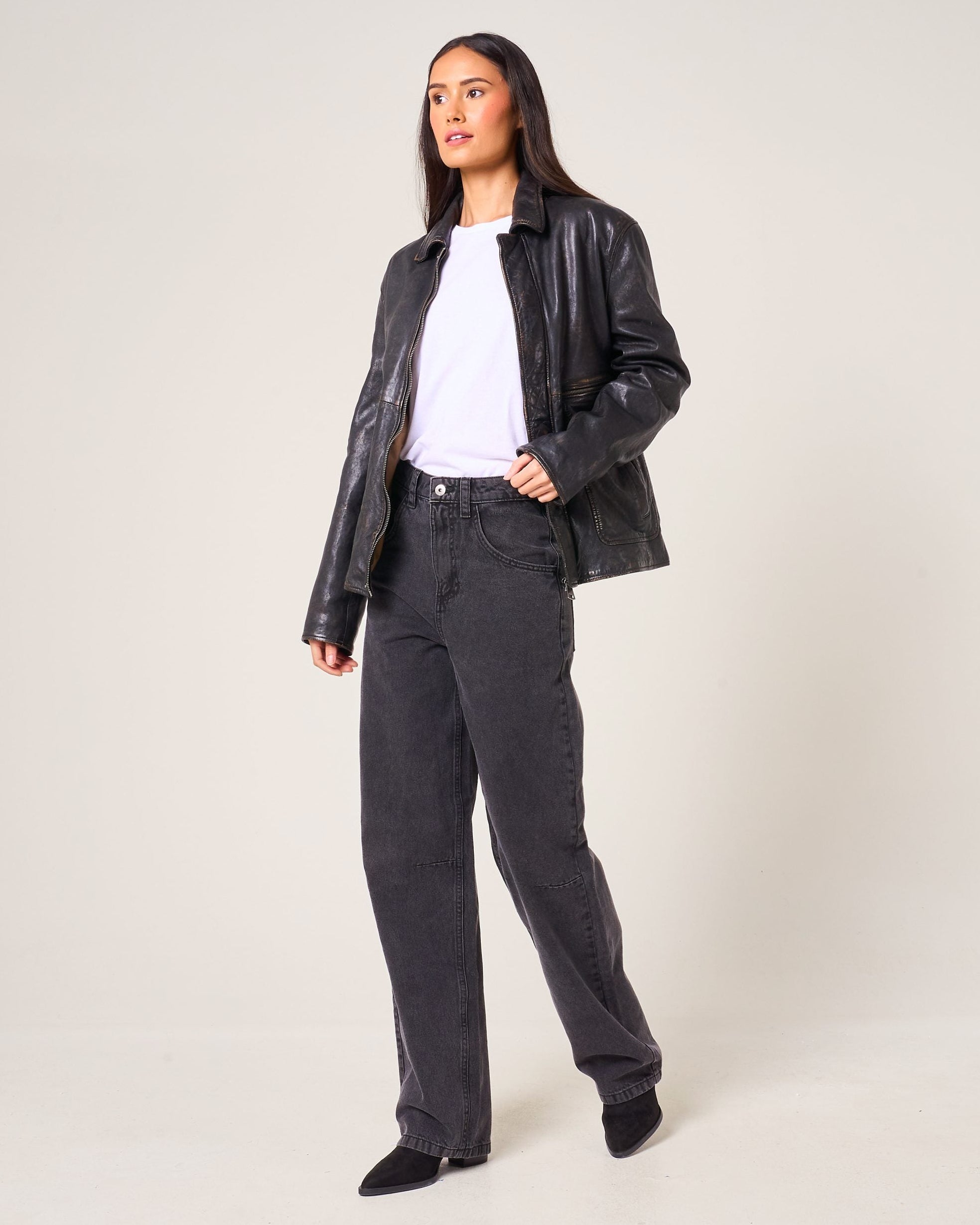Person wearing a black leather jacket and grey pants on a white background photo studio setting.