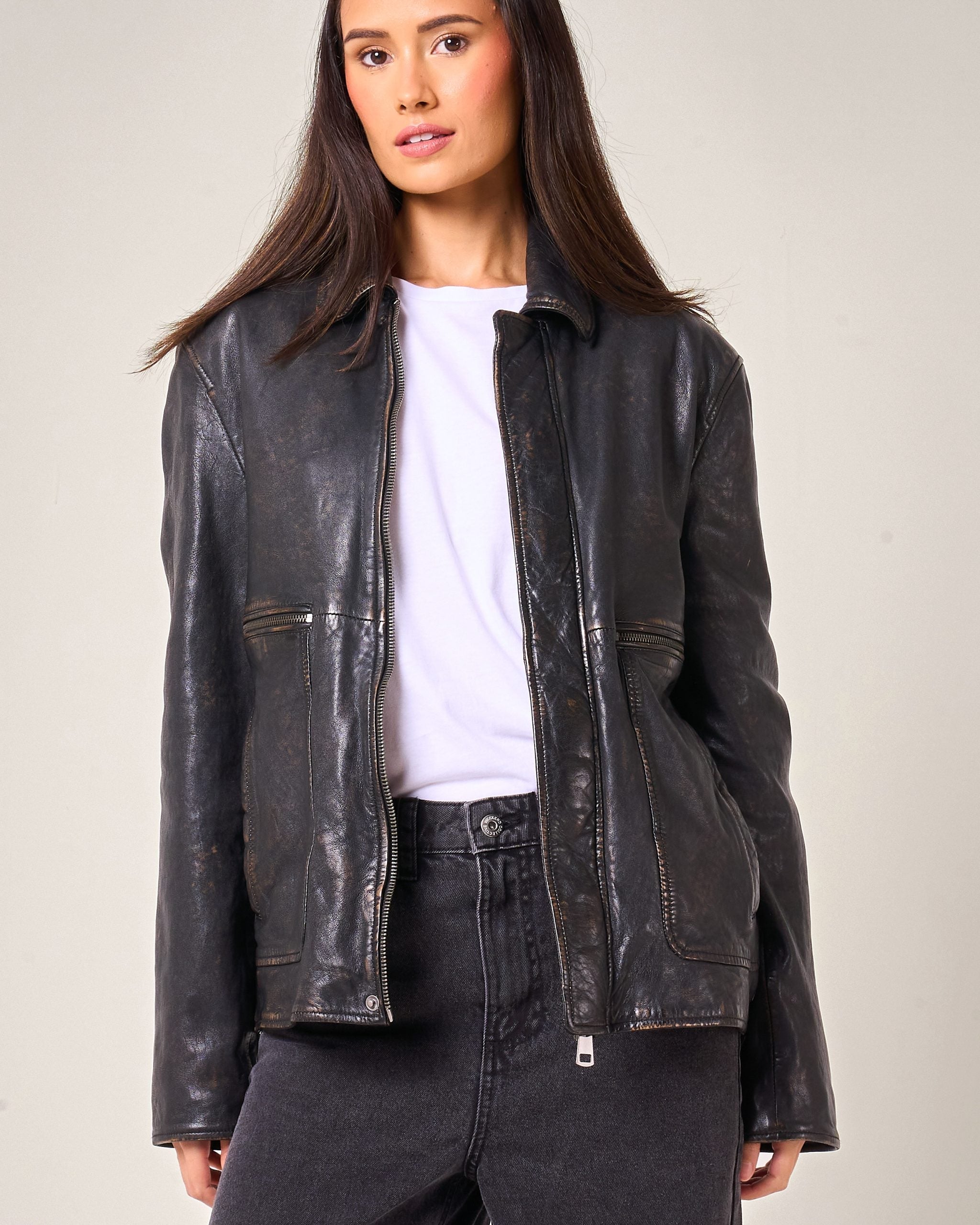 Woman wearing a black leather jacket on a plain background. Front of jacket has two zip pockets.