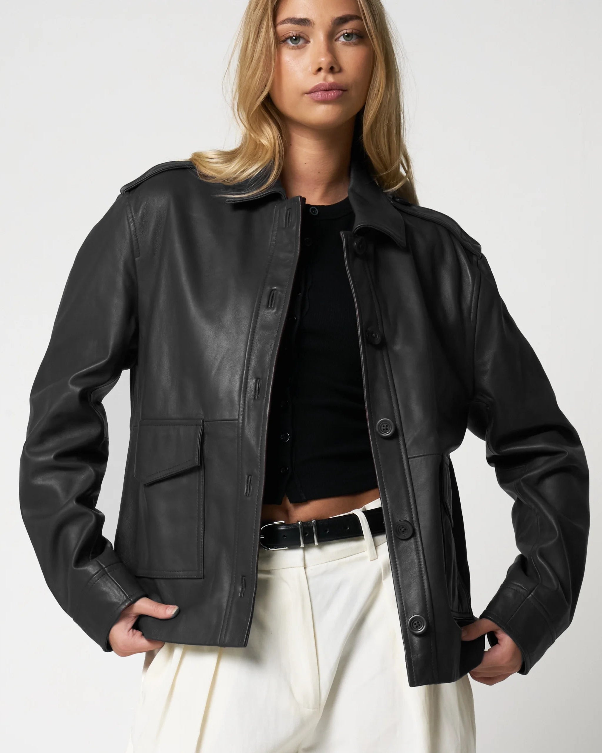 Woman wearing a black leather jacket on a plain background - the jacket has buttons and patch pockets.