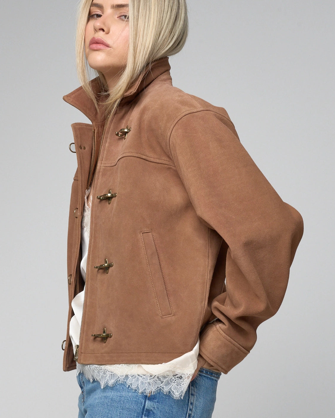Side view of woman wearing tan suede jacket with fireman clasps. You can see the welt pocket on the lower half of the jacket.