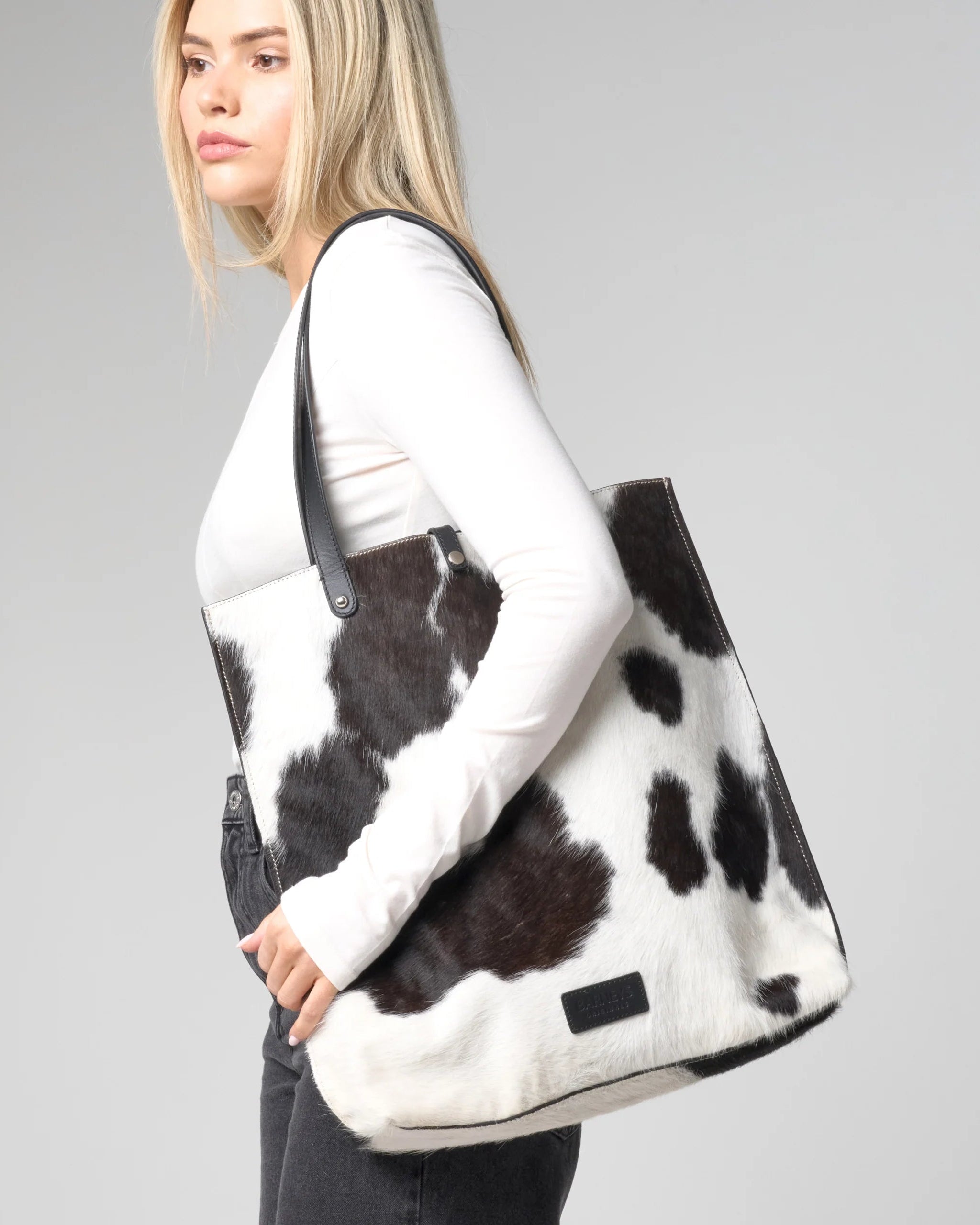 Woman wears a cow hide bag over her shoulder. The back is black and white with a natural cow print and hairy texture.