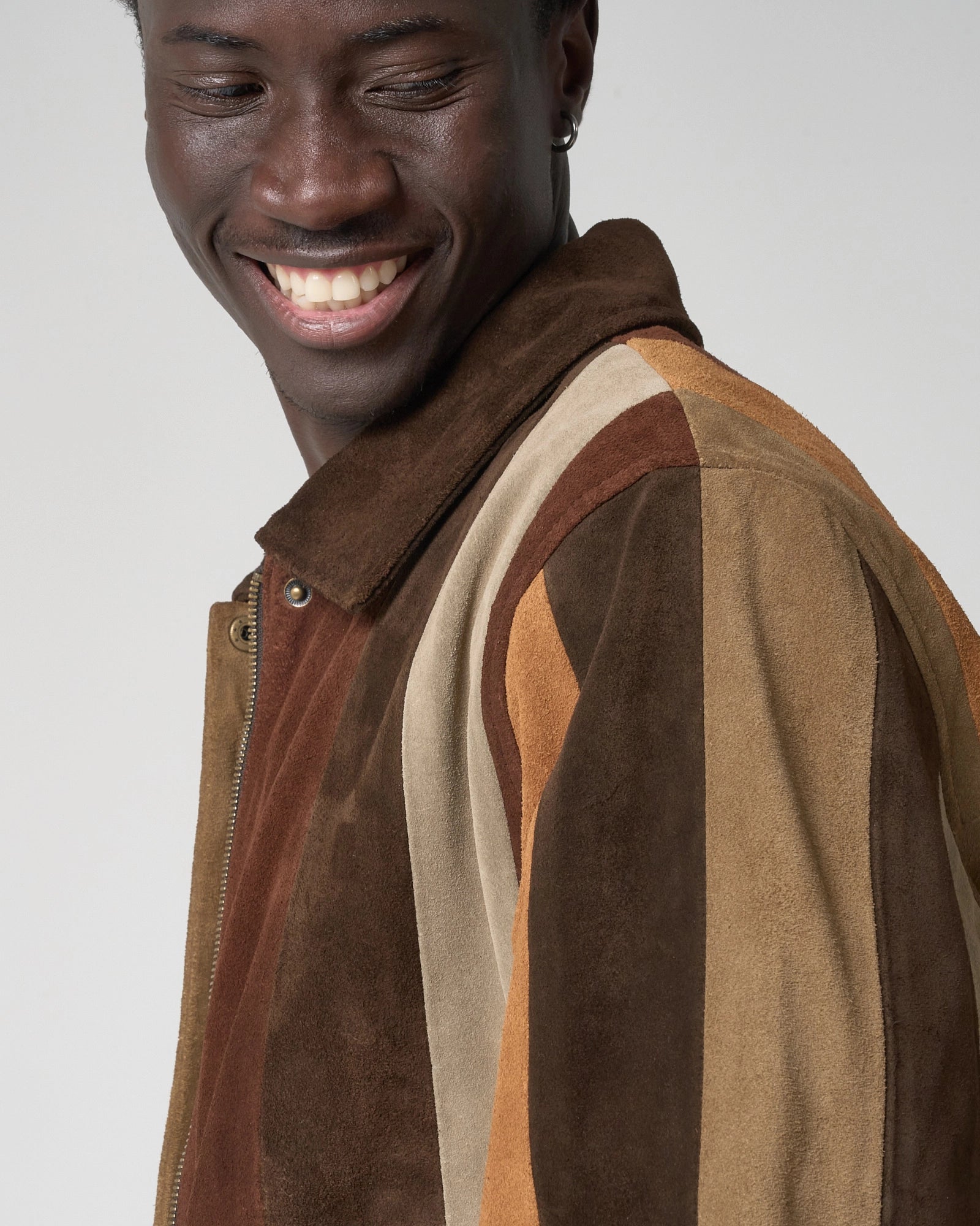 Image shows a close up image of a man wearing the striped suede bomber jacket by Barneys Originals. The shoulder and sleeve have a striped patchwork design.