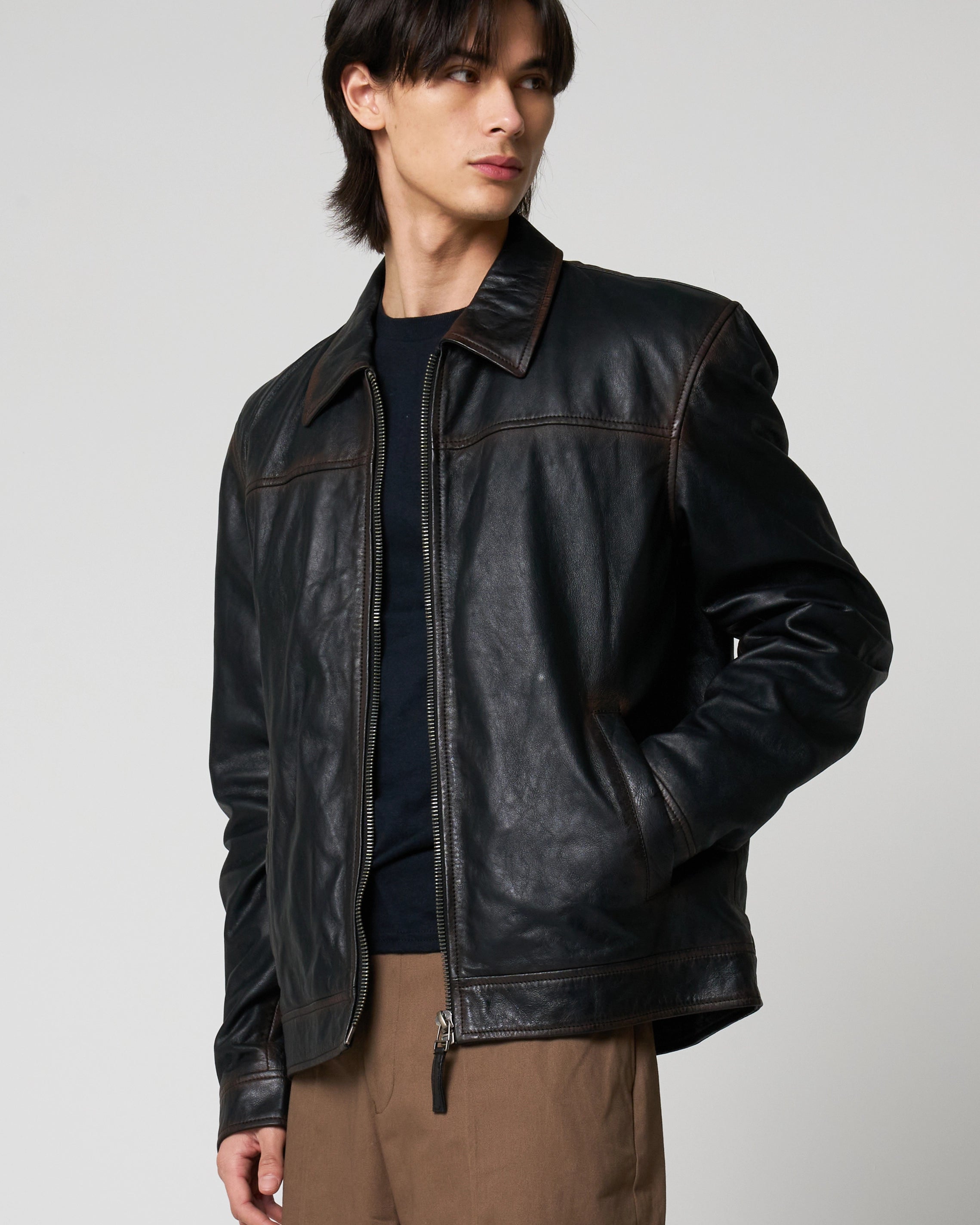 A man wearing a black leather jacket with contrast brown washed detail over a dark shirt and brown pants.