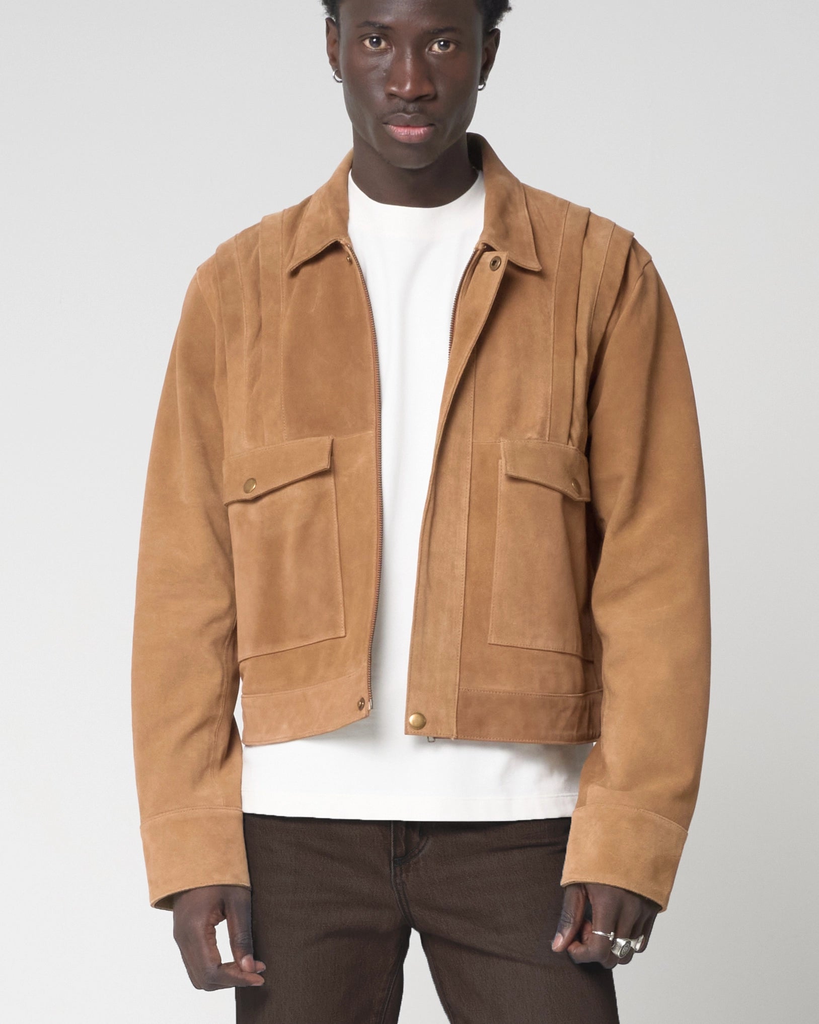 Image shows a man facing forward with the tan suede jacket unzipped. The jacket ends at the waistline and has a cropped fit. 