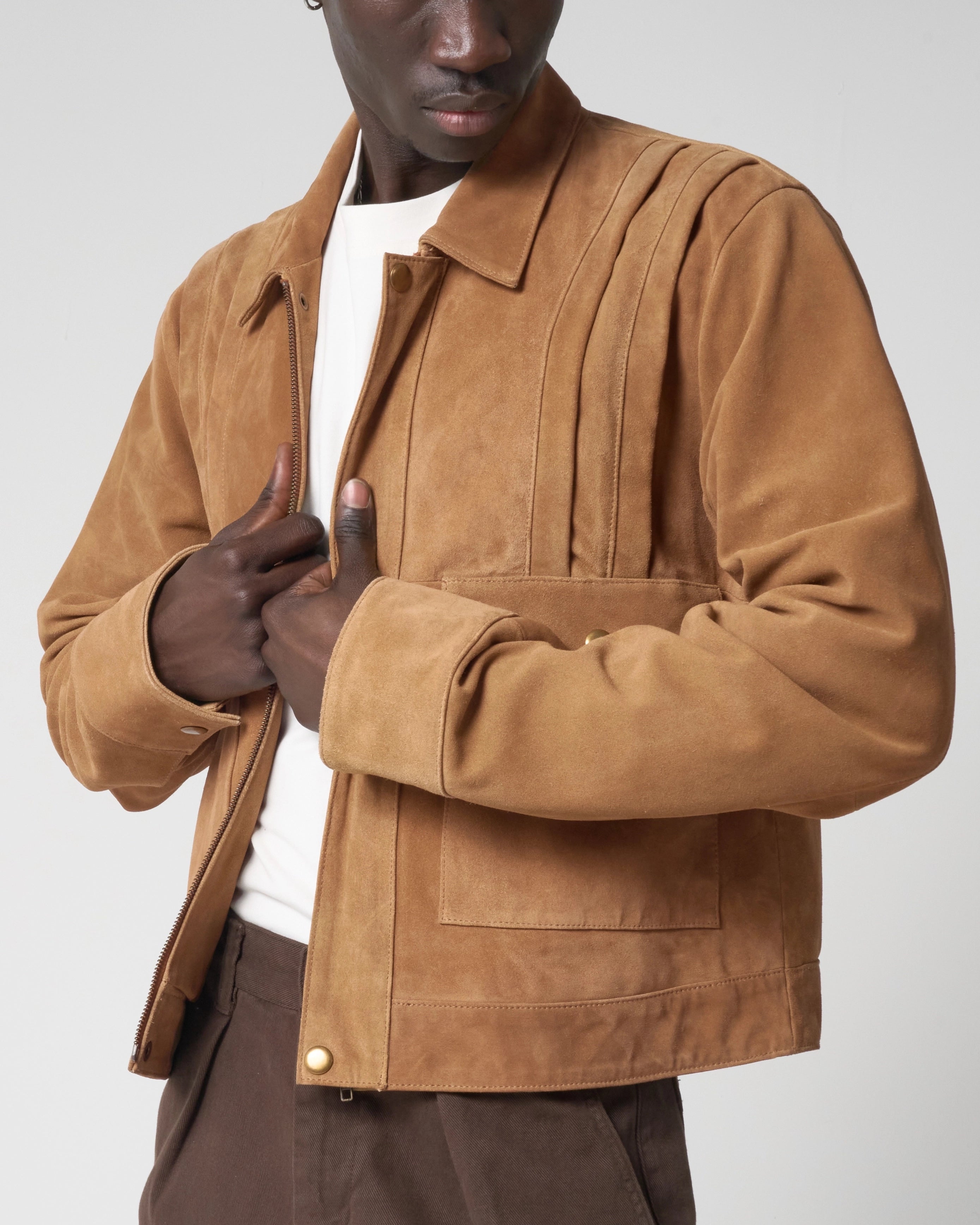 Detail image ighlighting the pleated detail and cropped fit of the tan suede jacket The model holds the zipline of the jacket.