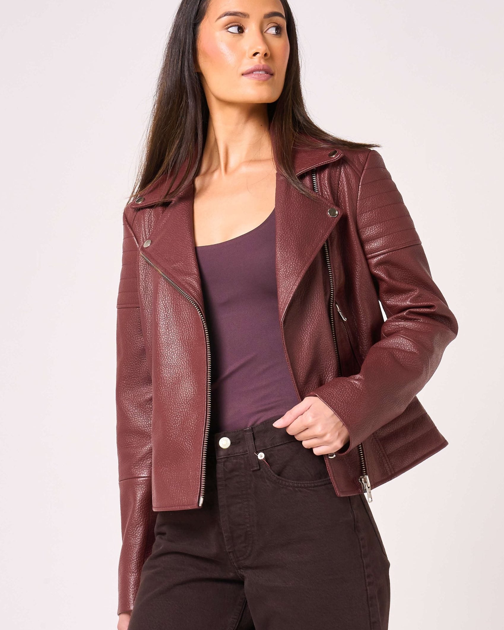 Woman wearing a burgundy leather jacket with asymmetric zipline and ribbed shoulder detail.
