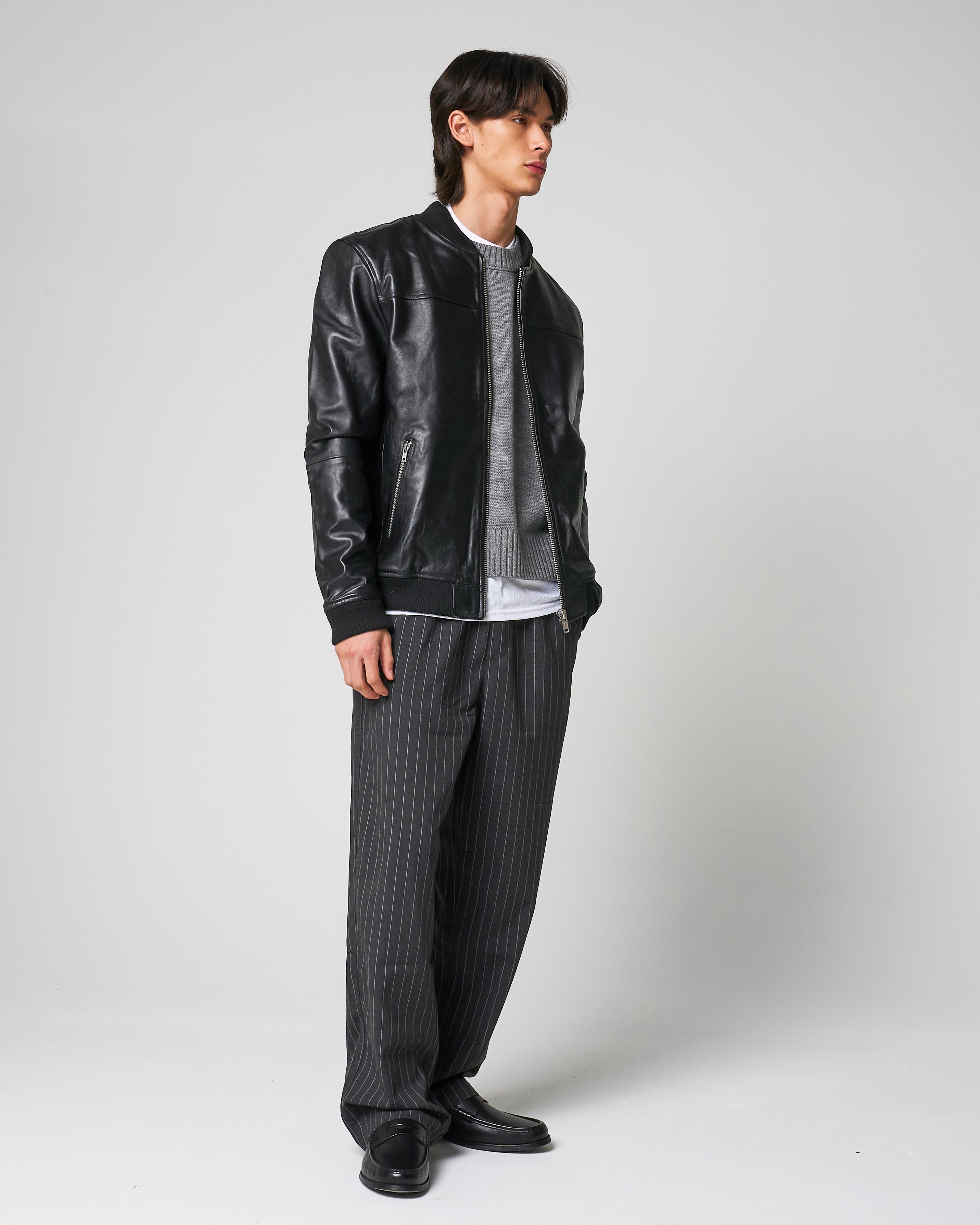 Full outfit image shows the real leather jacket worn by a male model, the jacket is styled with grey pinstripe trousers, loafers and a grey sweater.
