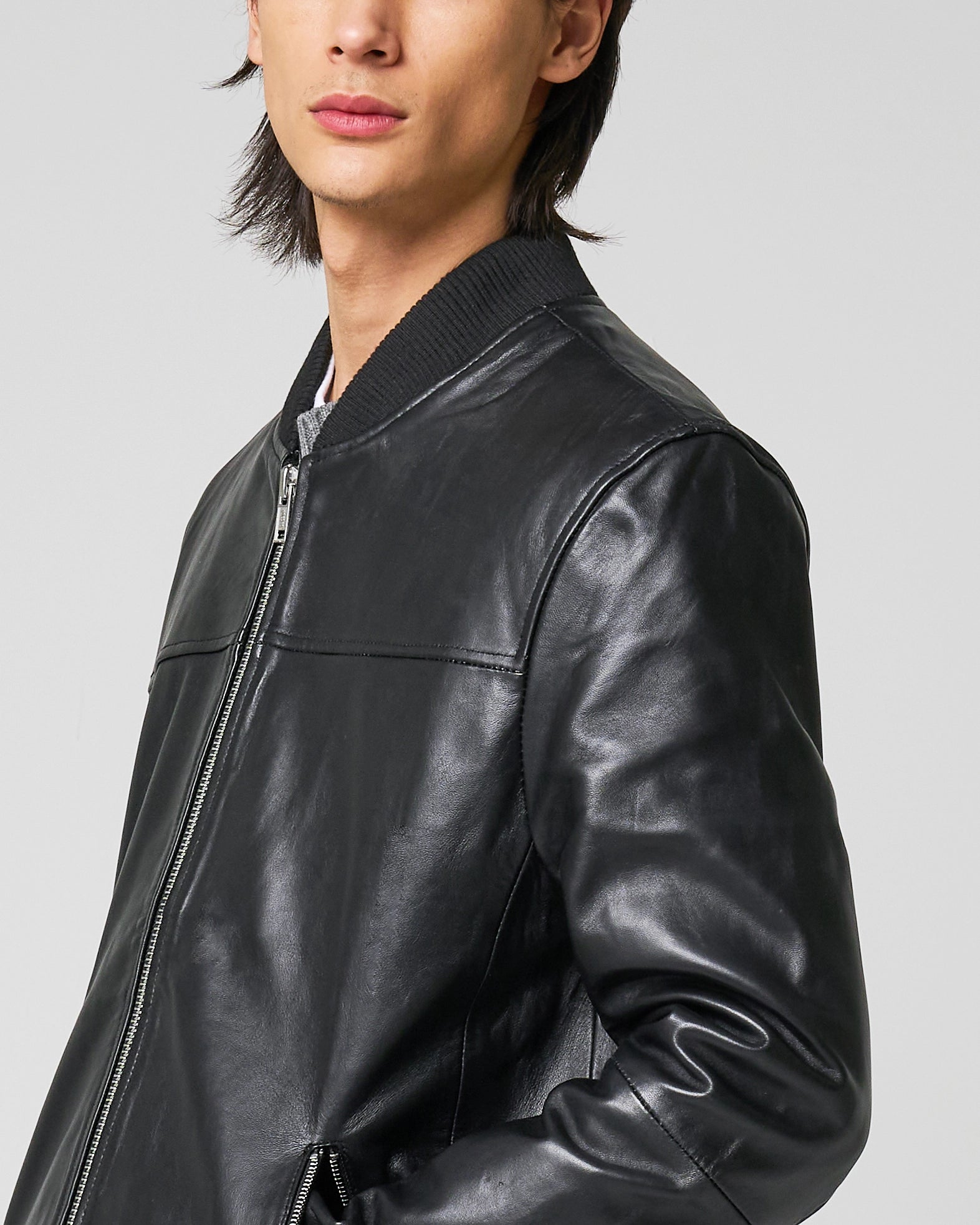 Close up image of male model wearing the real leather bomber jacket focusing on the neckline which has a knit rib. The leather has a smooth texture.