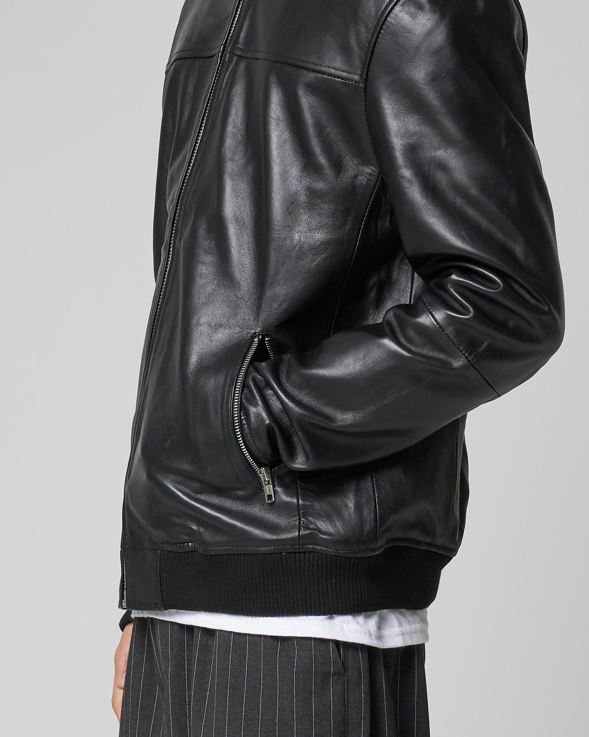 Close up detail shot of real leather bomber jacket as worn by a man, he puts his hands in the pocket which features a silver zip.