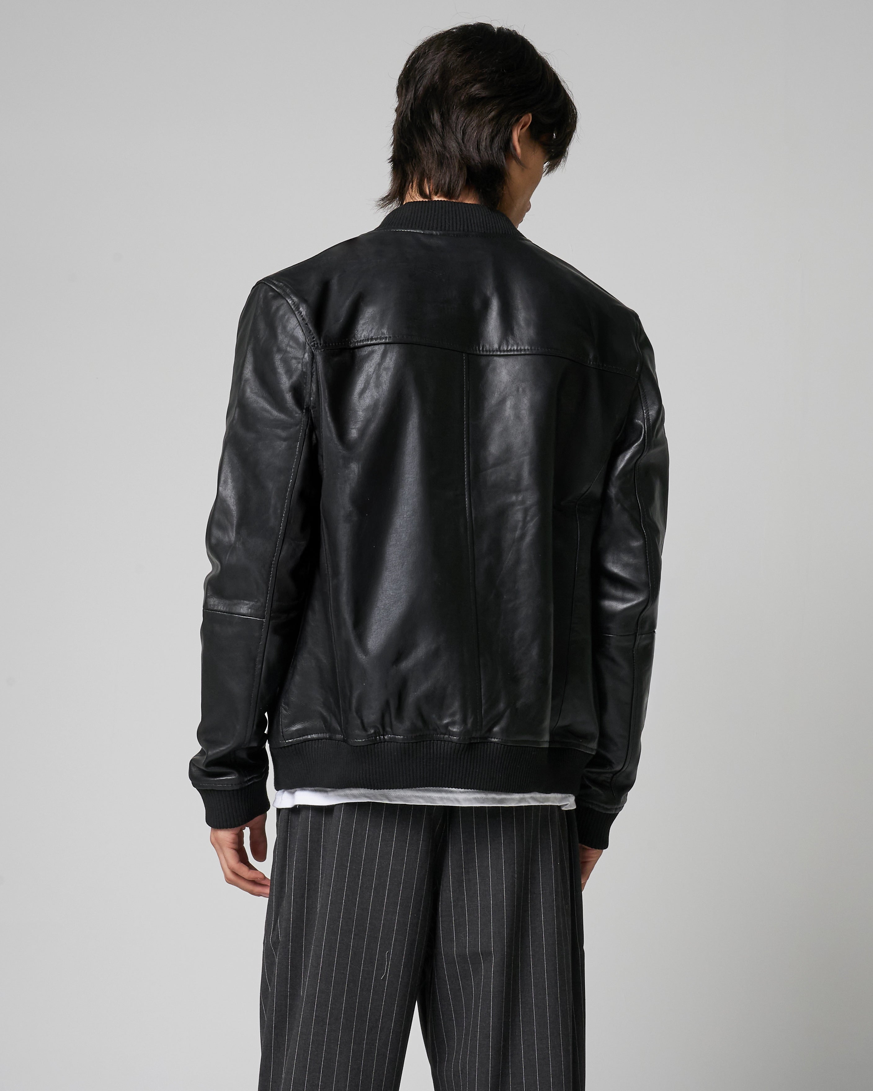 Back of real leather bomber jacket as worn by a man. The jacket is black in colour with no pattern or logos, with a knit rib hem and cuffs.