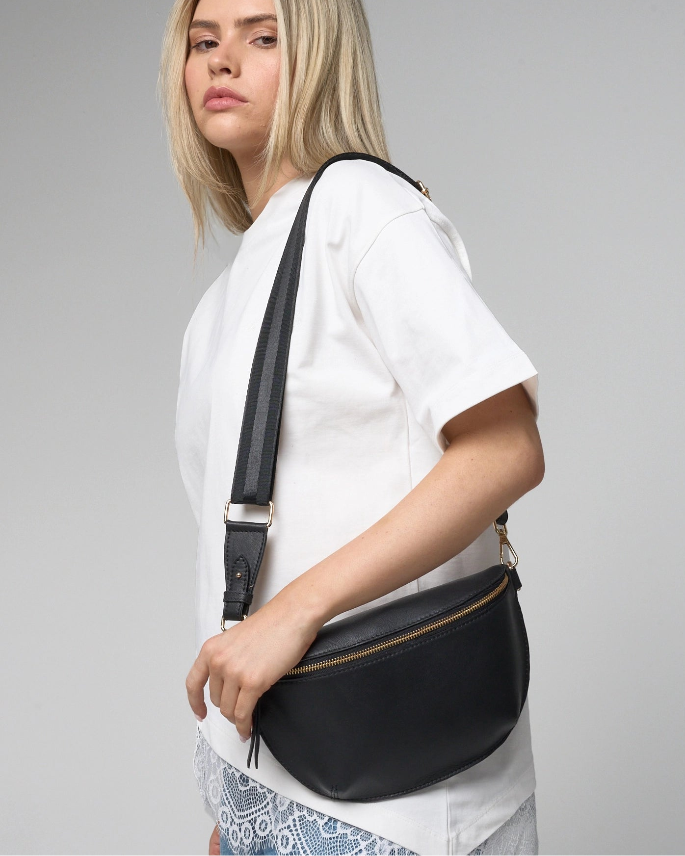 Woman wearing a black crossbody bag against a gray background