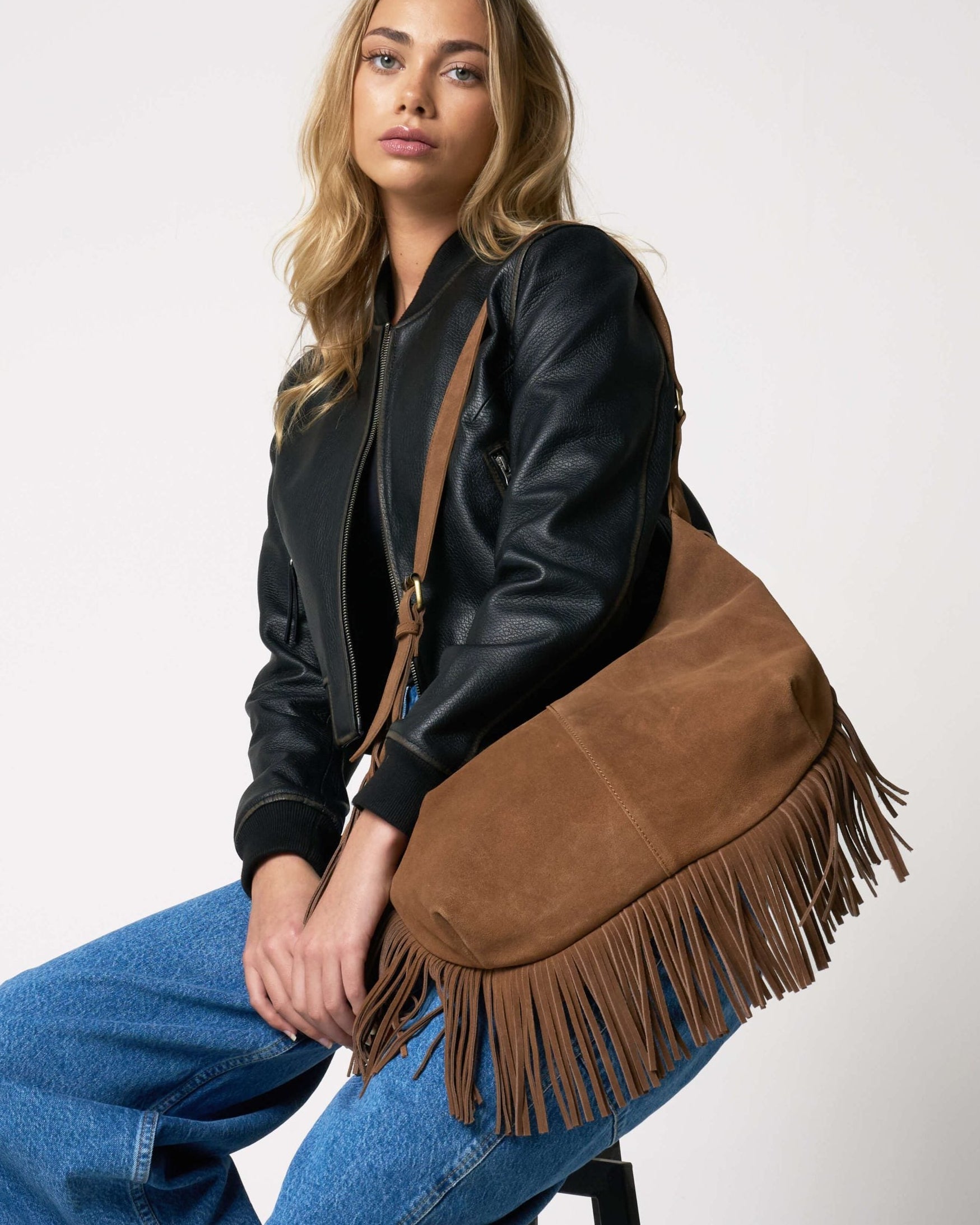 Woman holding a brown suede bag with fringes on a white background
