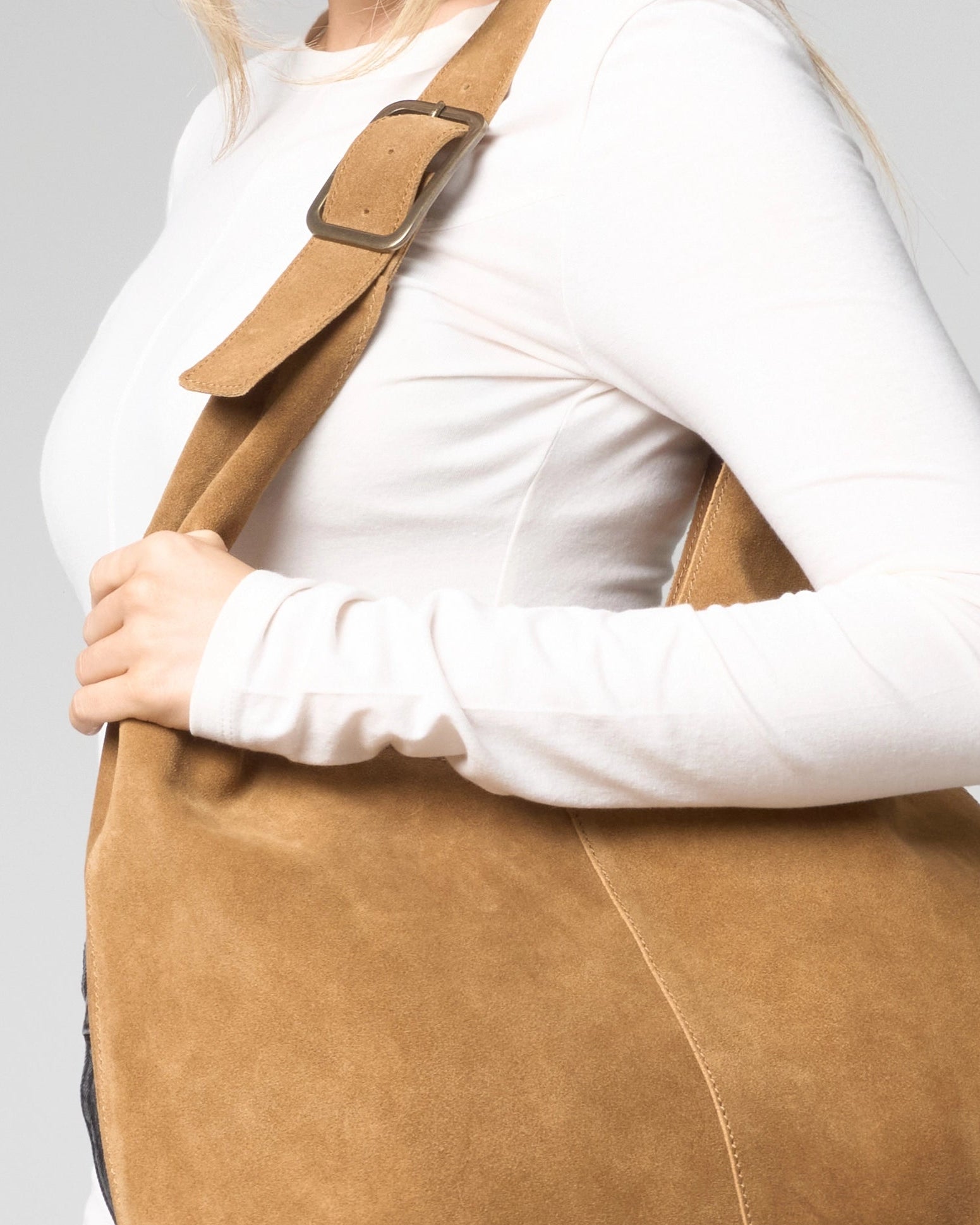 Close up detail image of the suede slouch bag. The suede has a soft, fine grain appearance. The strap of the bag has a brass buckle.