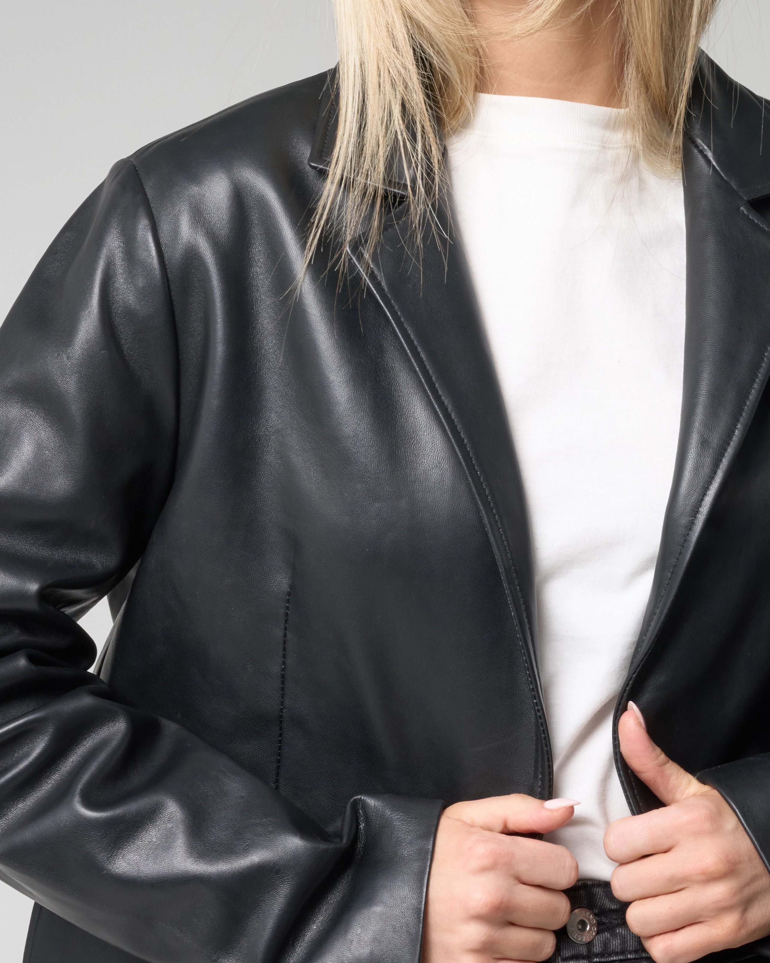 Cropped action shot of woman wearing the leather blazer, pulling the jacket closed over her outfit.