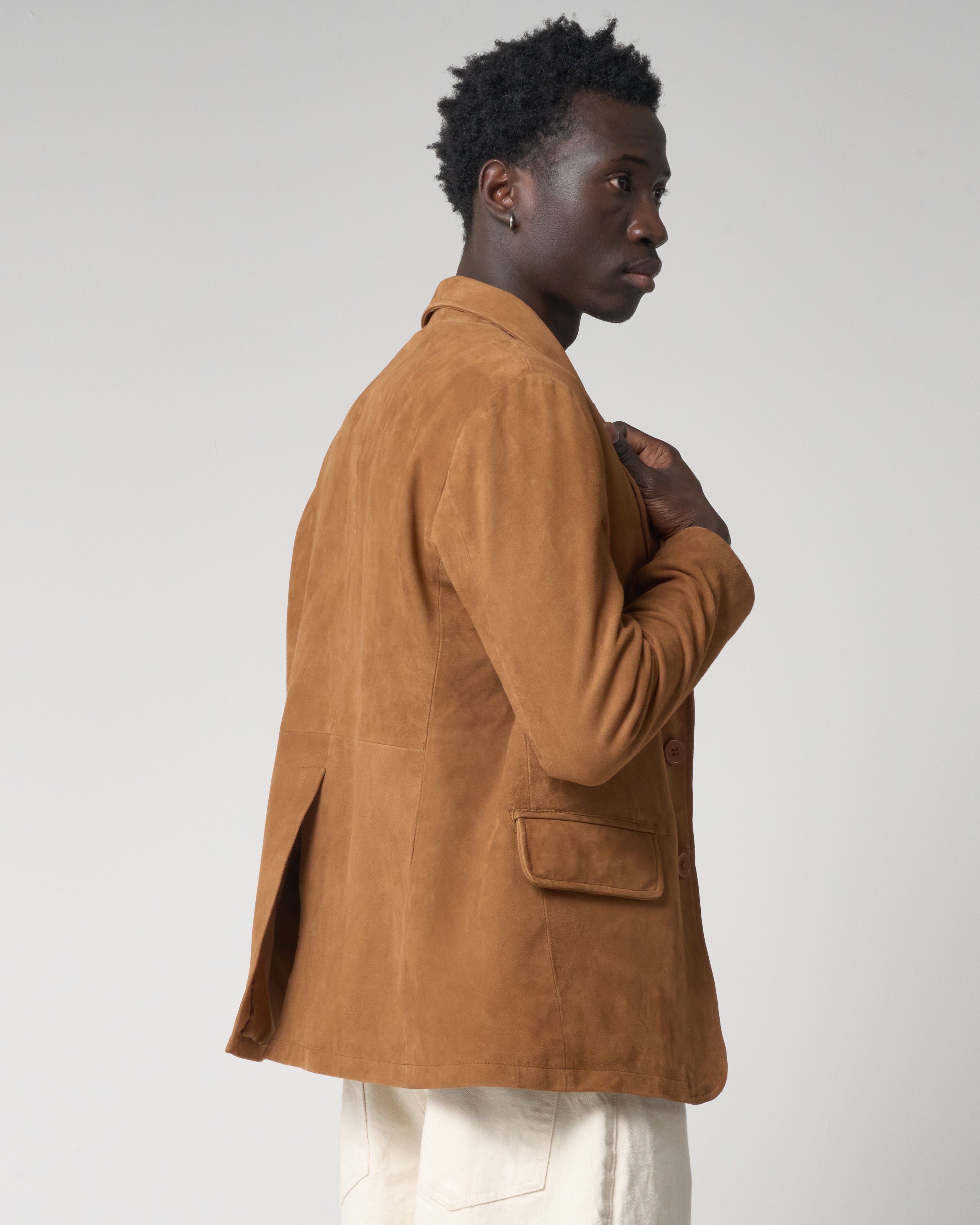 Side profile image of a man wearing a real suede blazer jacket that is tan in colour. The jacket has pockets, no pattern or external brand logos.