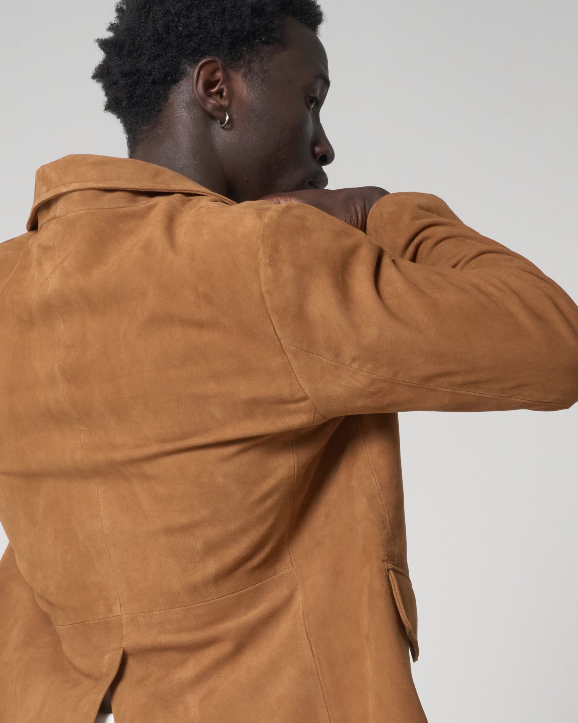 Action shot of the back of the blazer as worn by a male model. The man adjusts his collar.