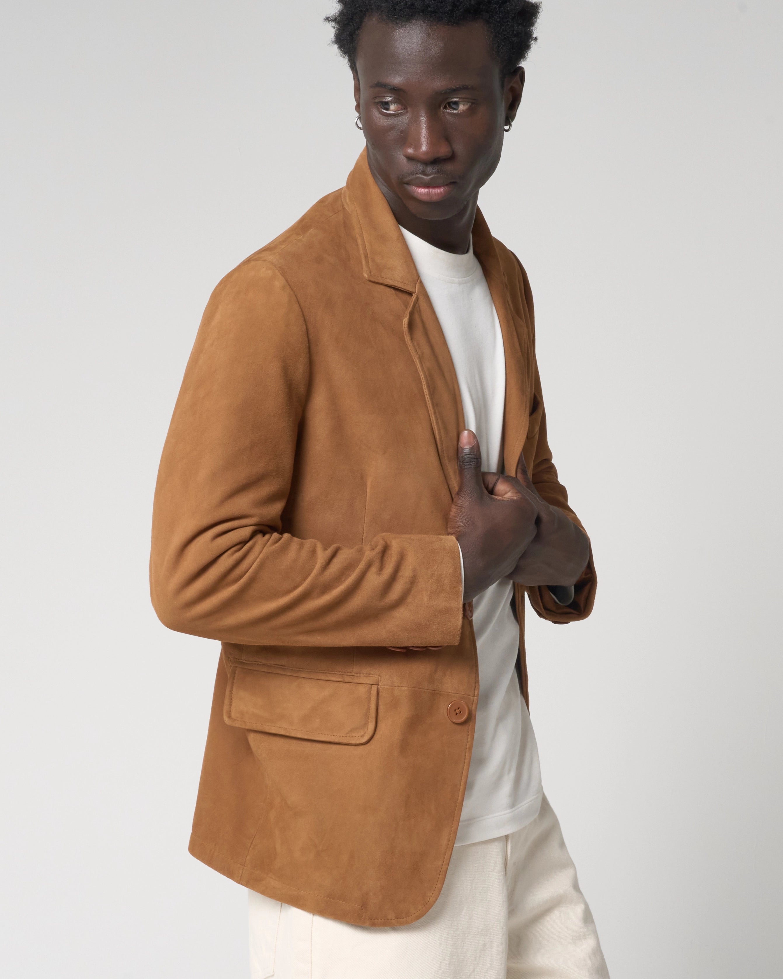 A man wearing a tan real suede blazer over a white t-shirt and cream trousers.