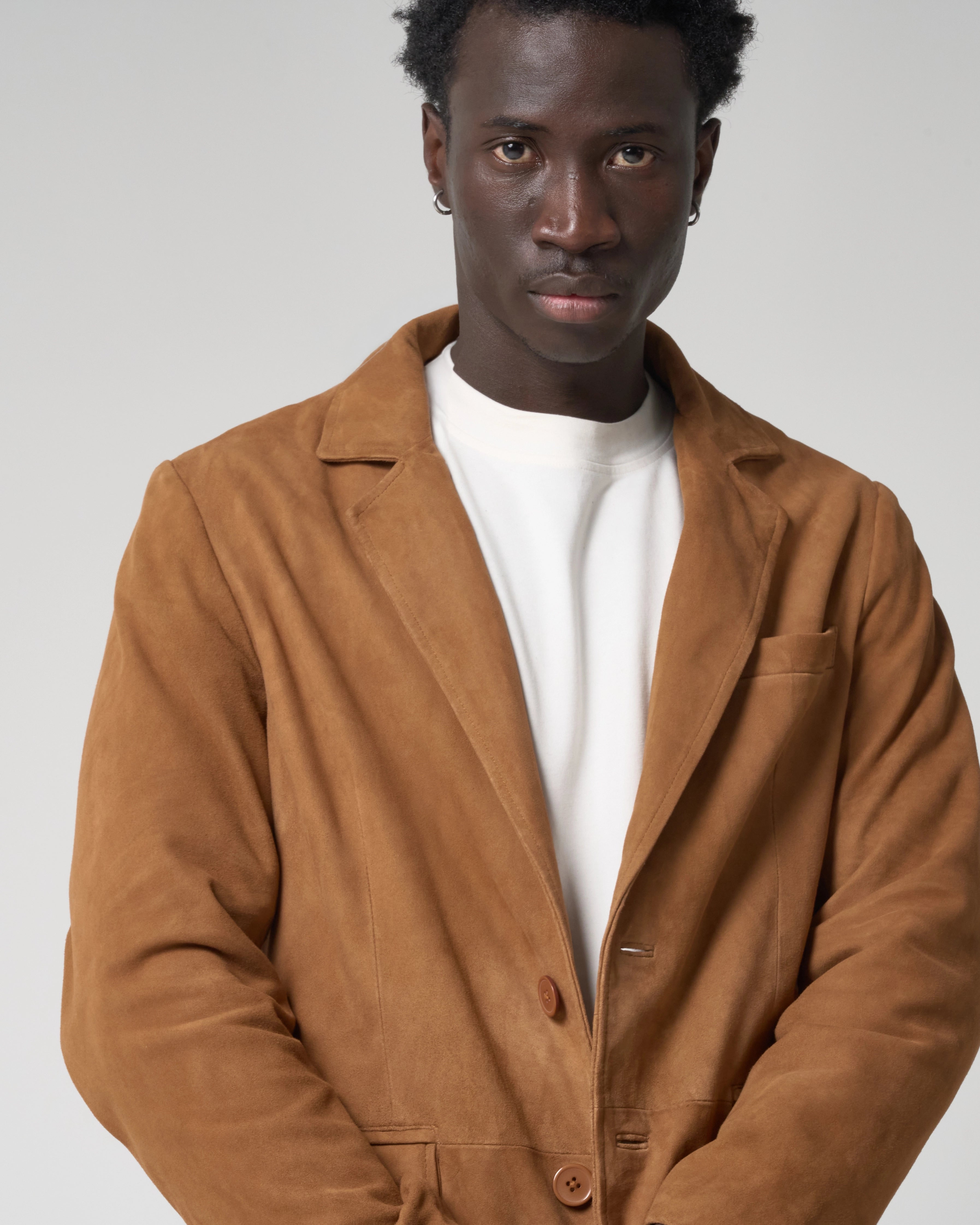 Man wears a tan suede blazer jacket with smooth texture and buttons.