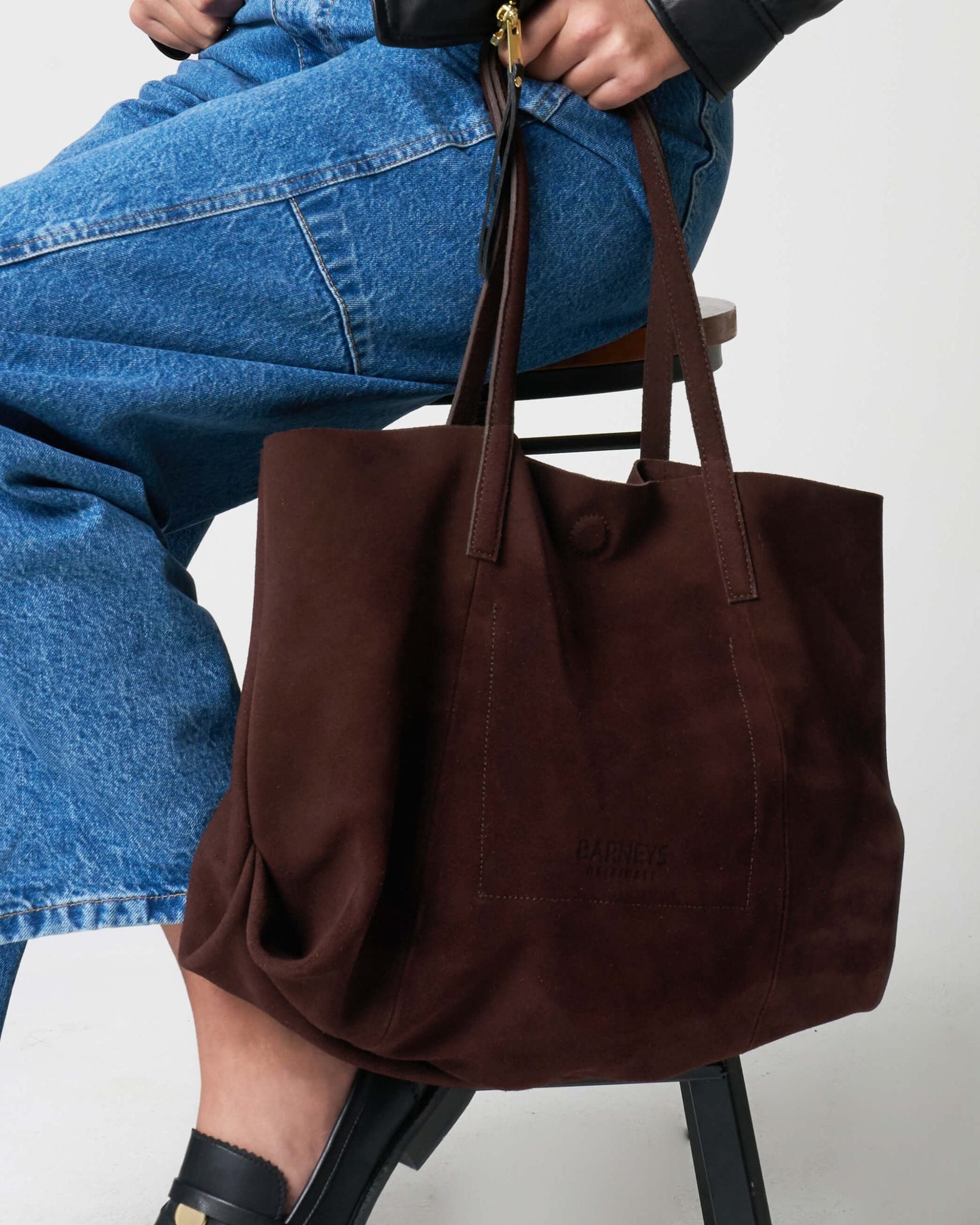 Brown tote bag held by a person wearing blue jeans on a white background