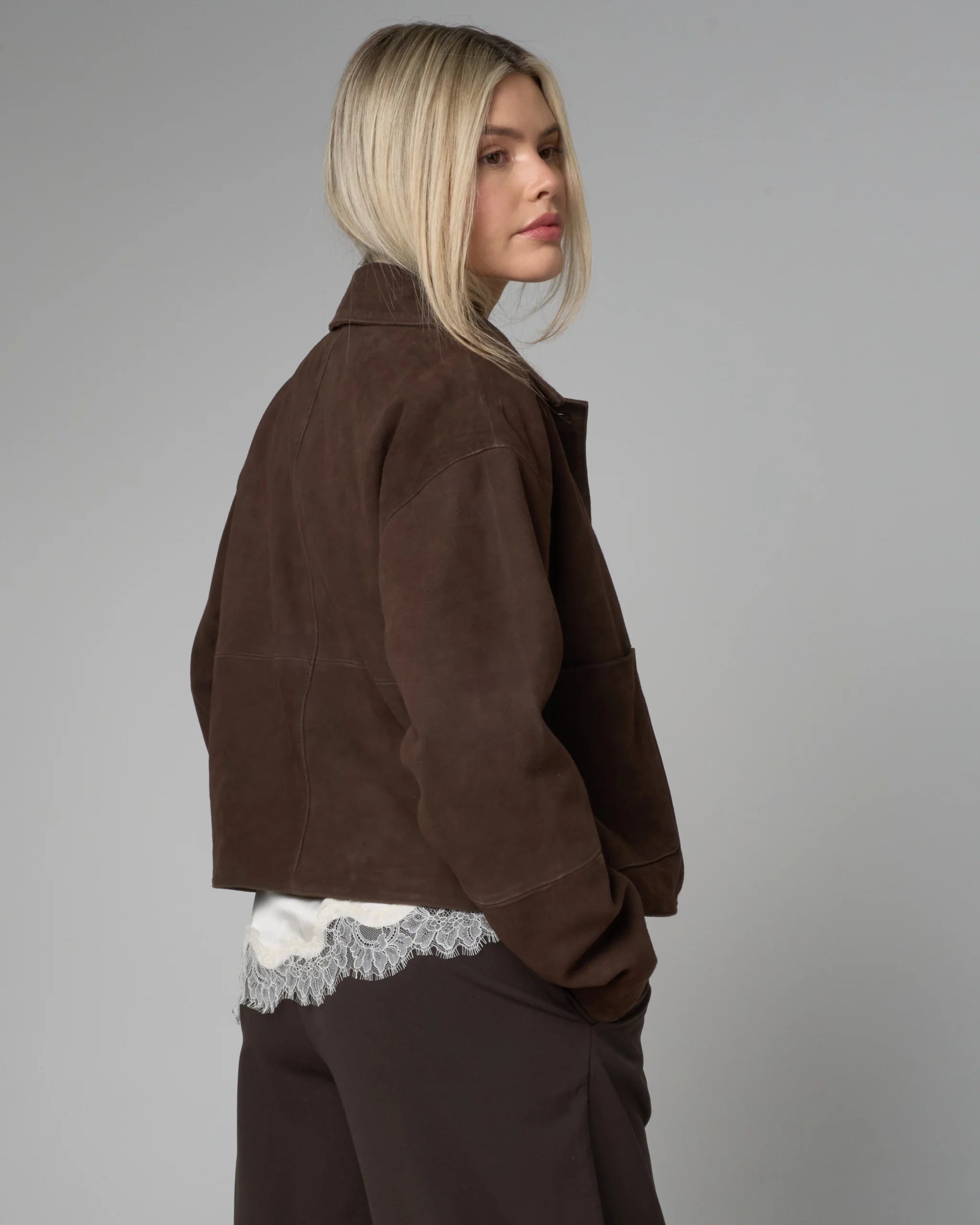 Woman wearing a brown suede jacket and pants against a gray background