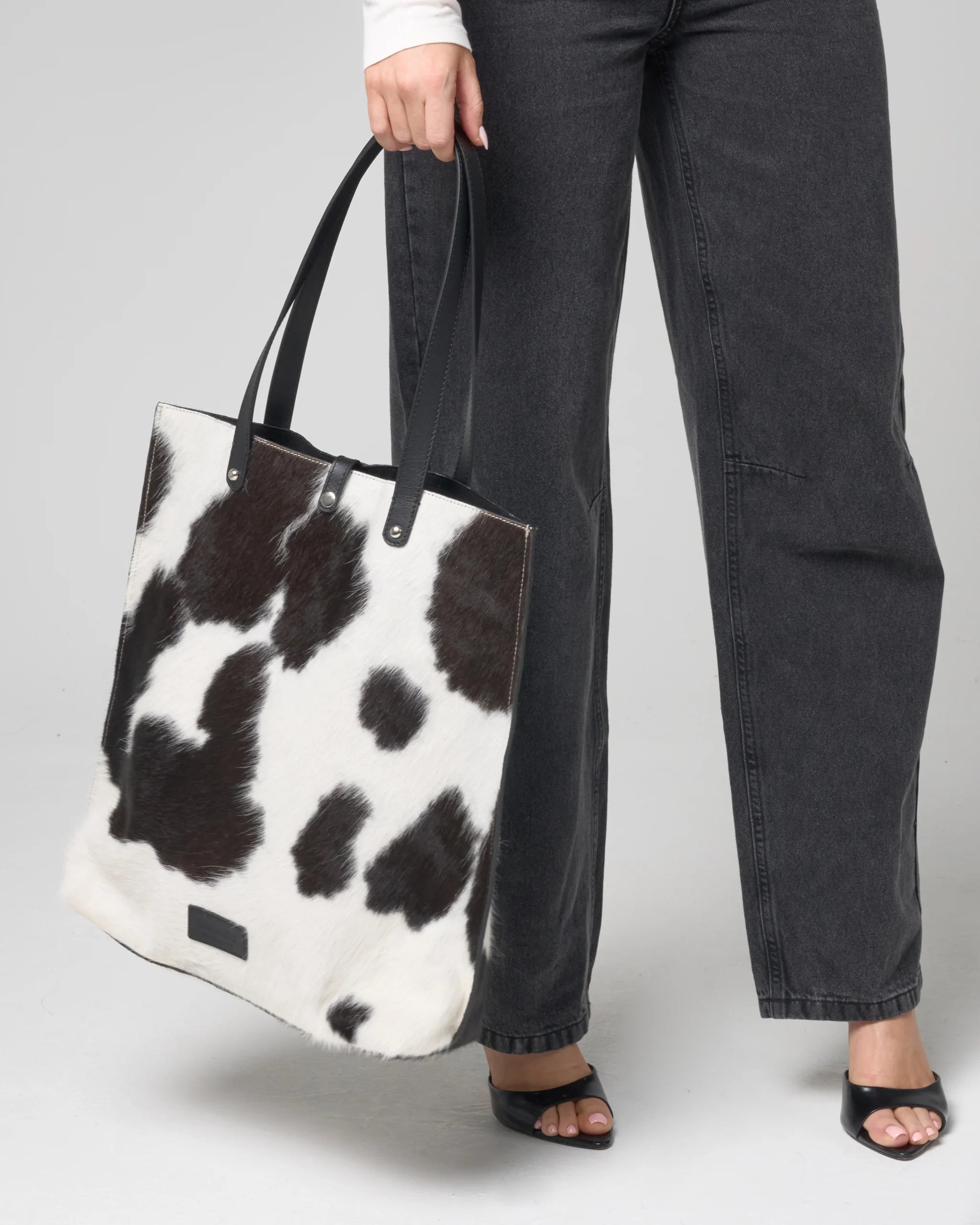 Person holding a cow print tote bag against a plain background
