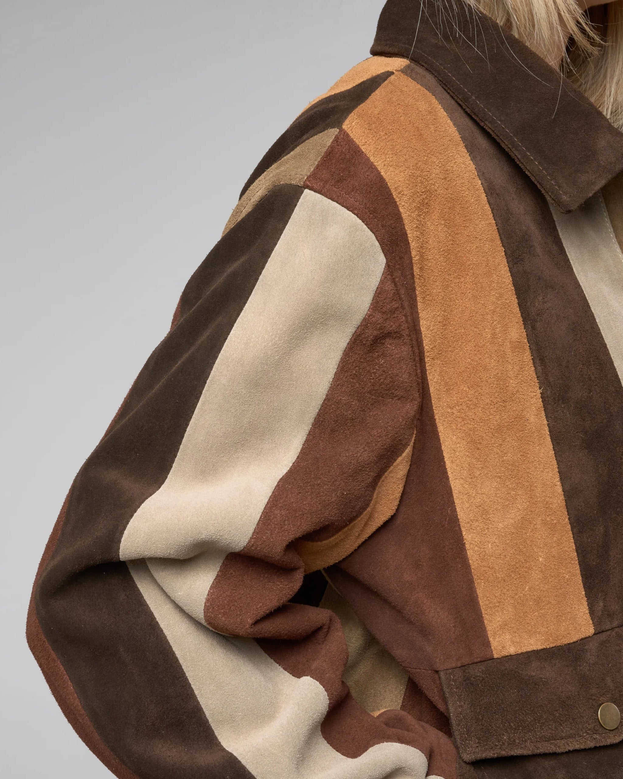 Close-up of a person wearing a brown, beige, and orange striped jacket on a grey background. Suede texture shown to have a fine fibrous appearance.