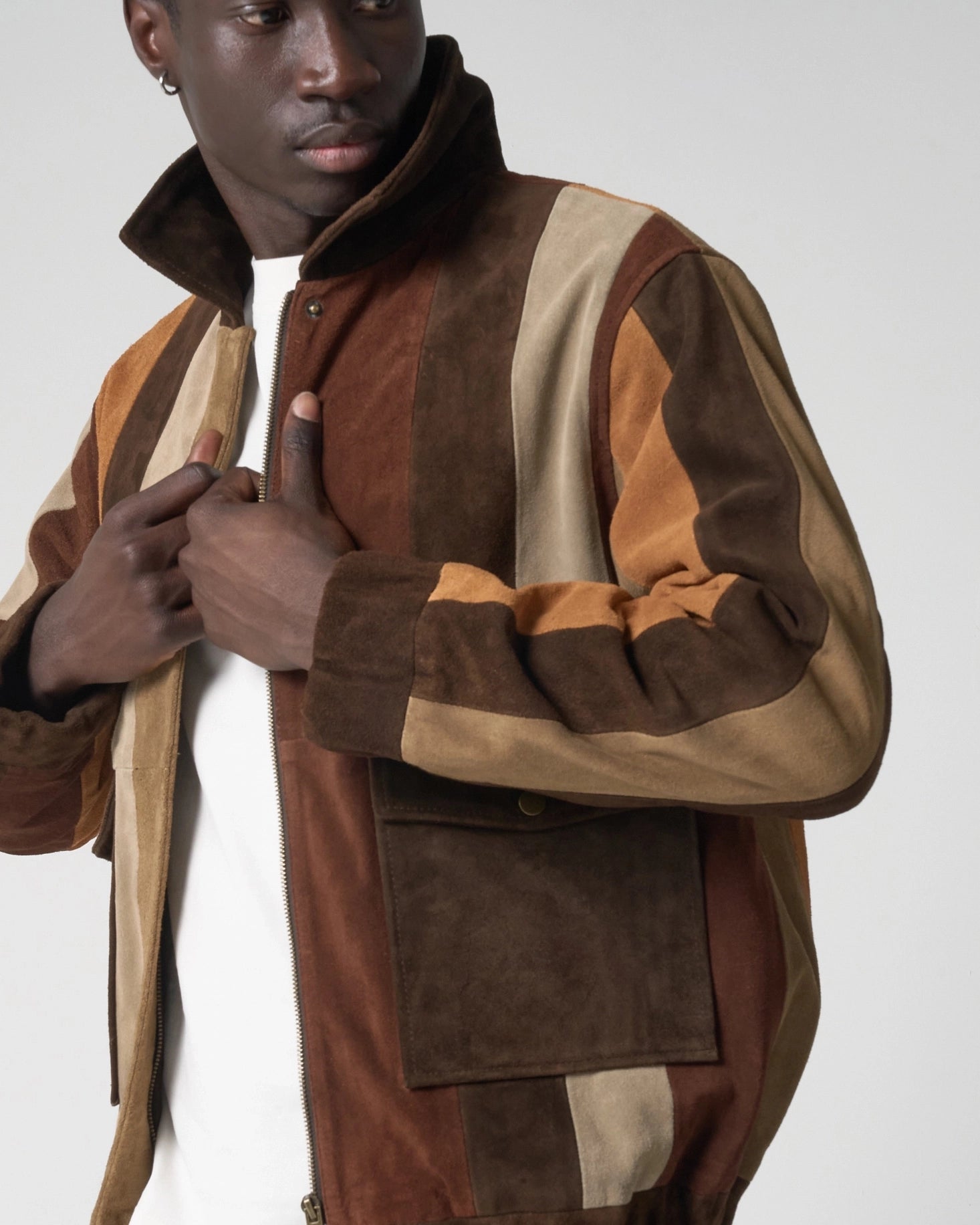 A man wearing a striped brown and beige colour-blocked suede jacket, with the collar popped up.