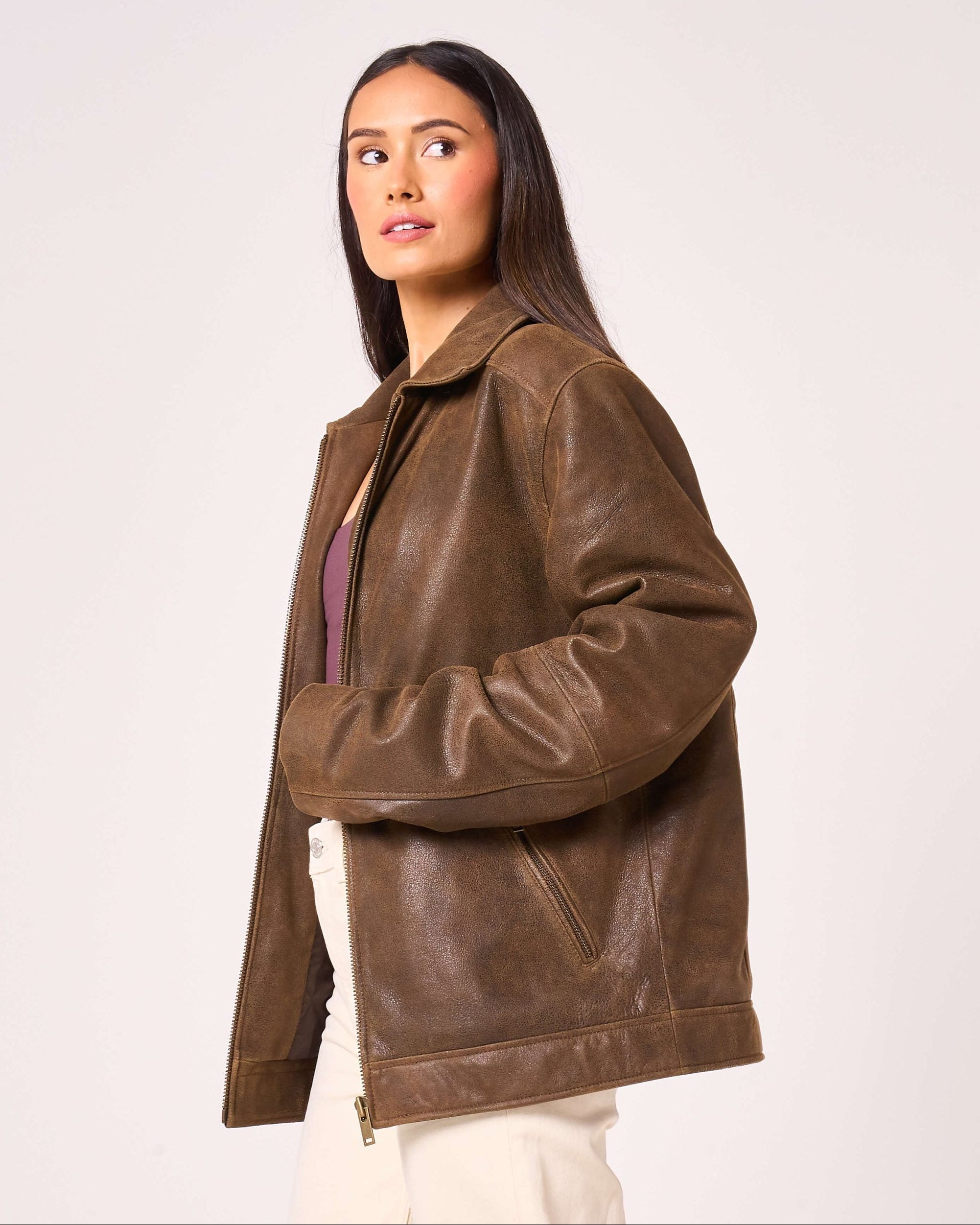 Woman wears oversized real leather jacket which is brown in colour. The sleeves are long and there is a central zipline.