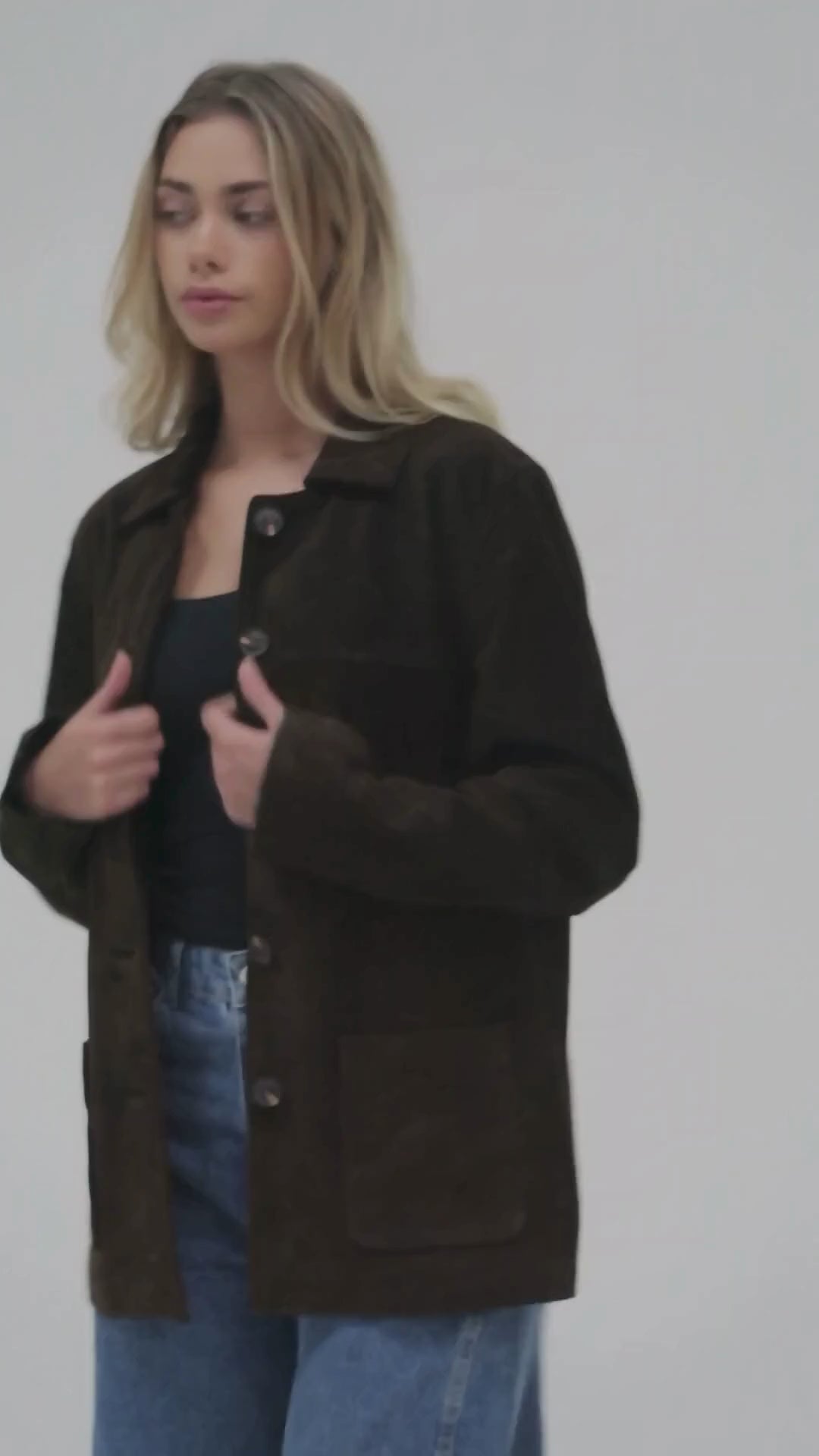 Image shows a blond woman styling the brown suede jacket in a white studio.