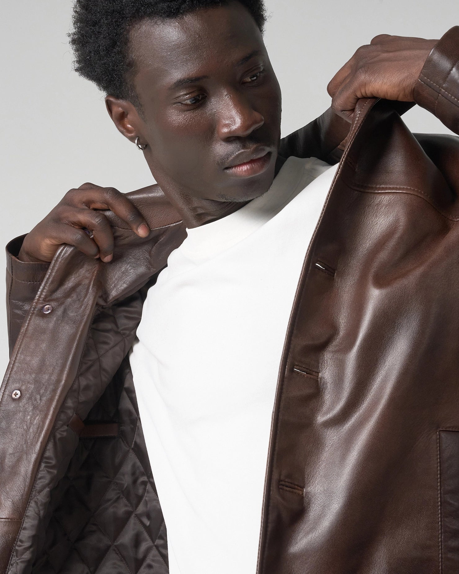 Image shows an action shot of a man putting on the brown leather jacket. The real leather is smooth in texture.
